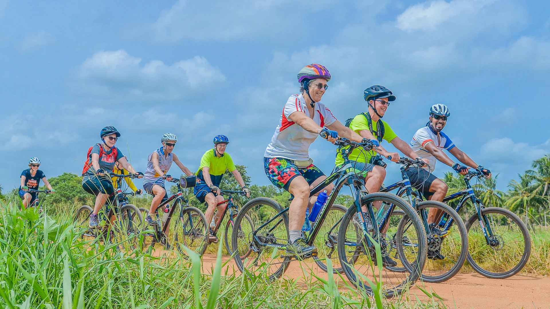 Group of cyclists riding along a red dirt path under a blue sky in rural Sri Lanka