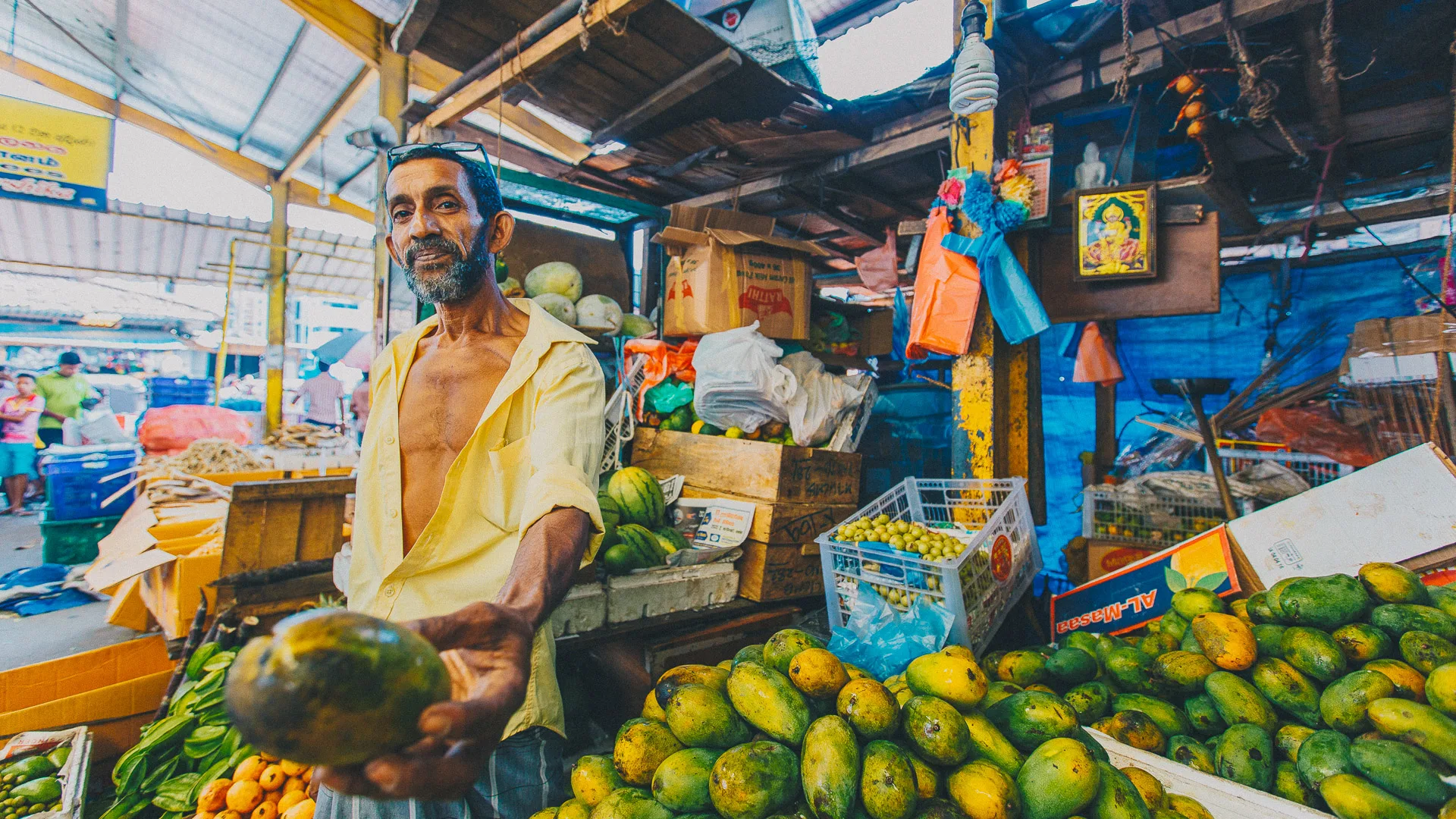 Man offering a ripe mango at a colourful market stall in Sri Lanka