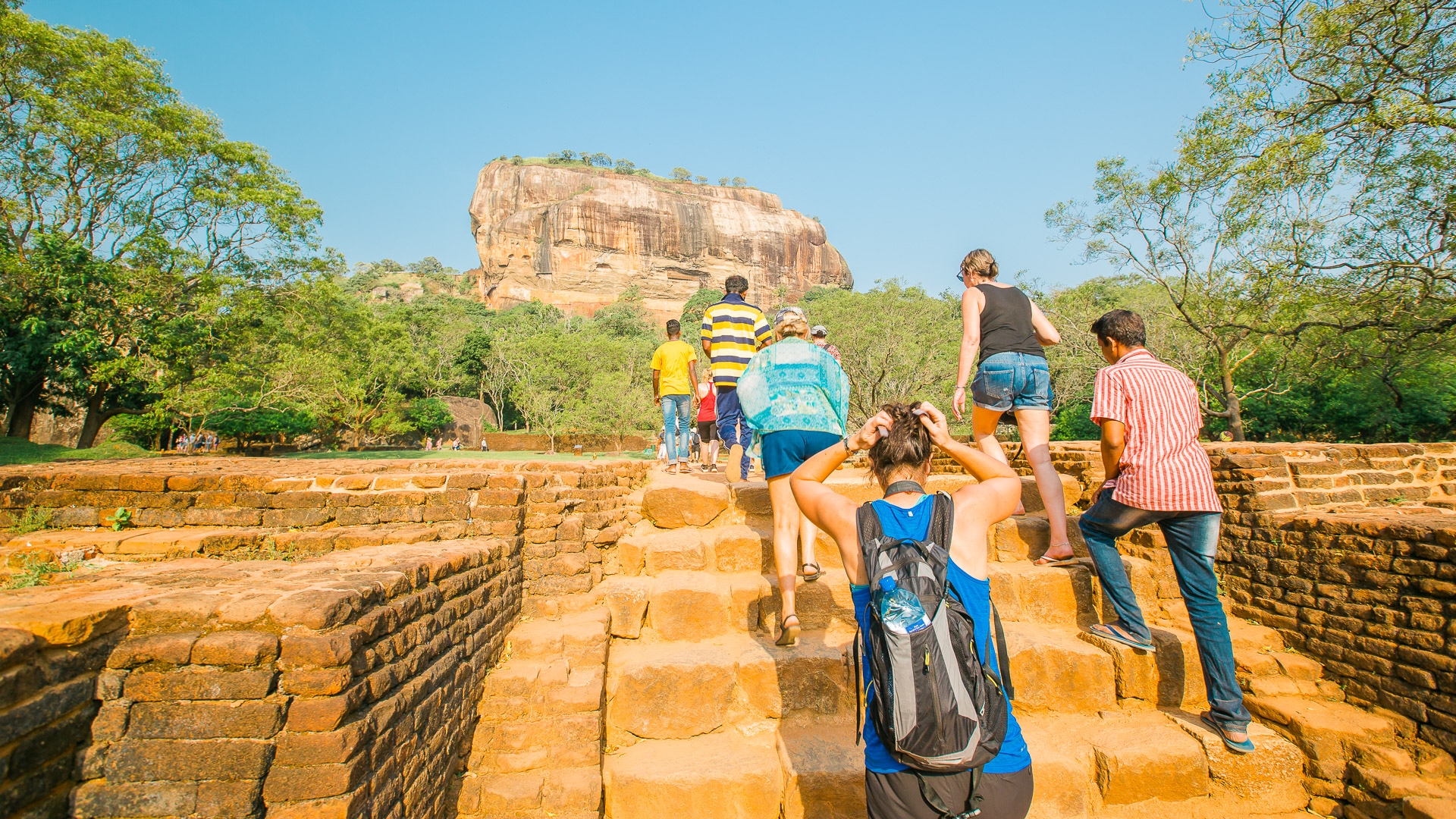 Group climbing steps toward Sigiriya Rock Fortress in Sri Lanka on a sunny day