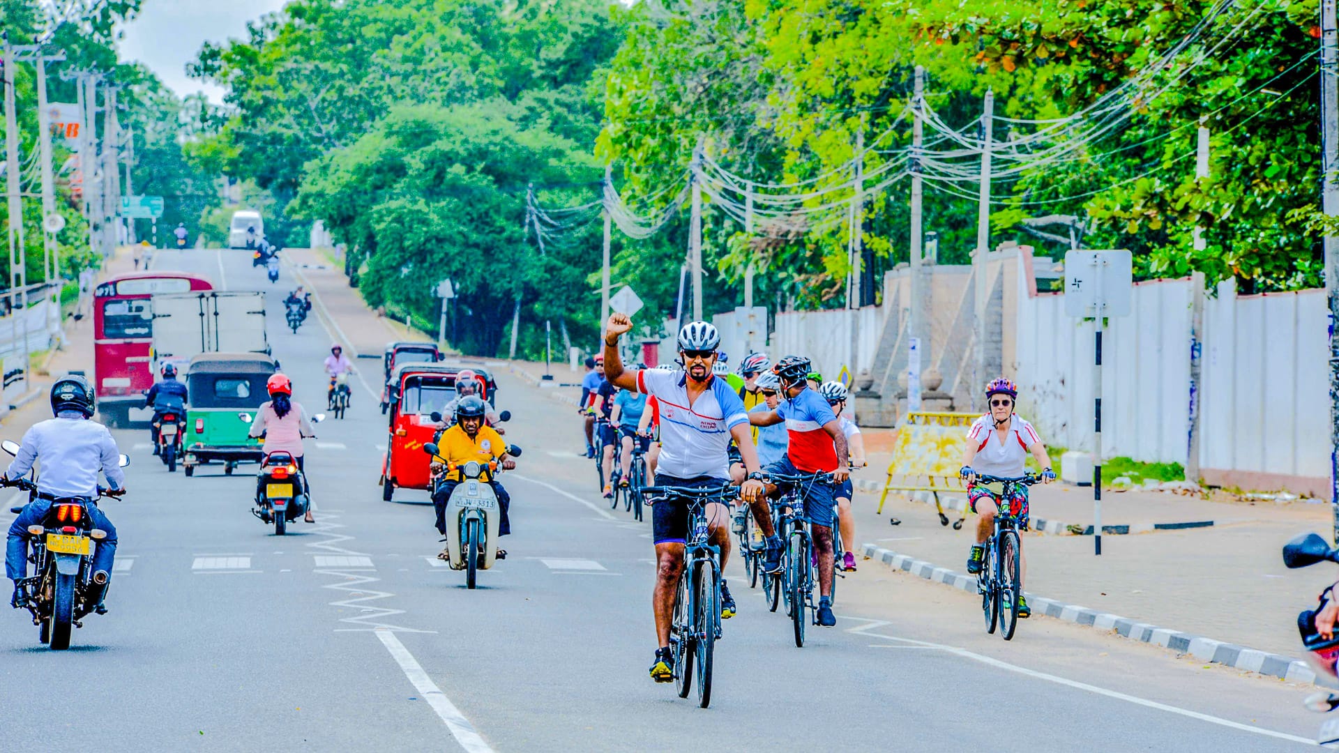 Cyclists riding through a busy street in Sri Lanka, surrounded by tuk-tuks, buses and motorbikes
