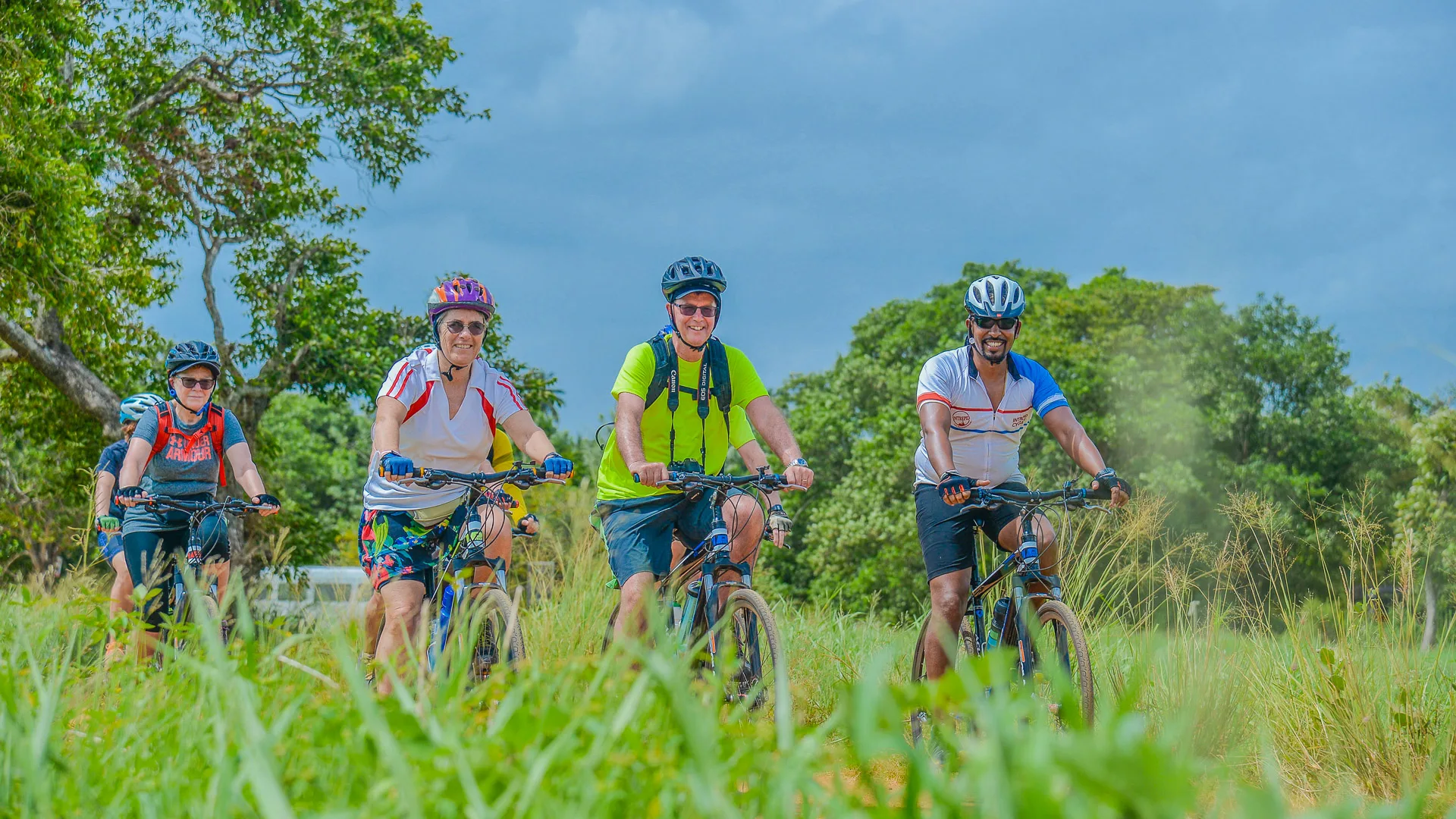 Group of cyclists riding through green landscape in Sri Lanka under a bright, cloudy sky