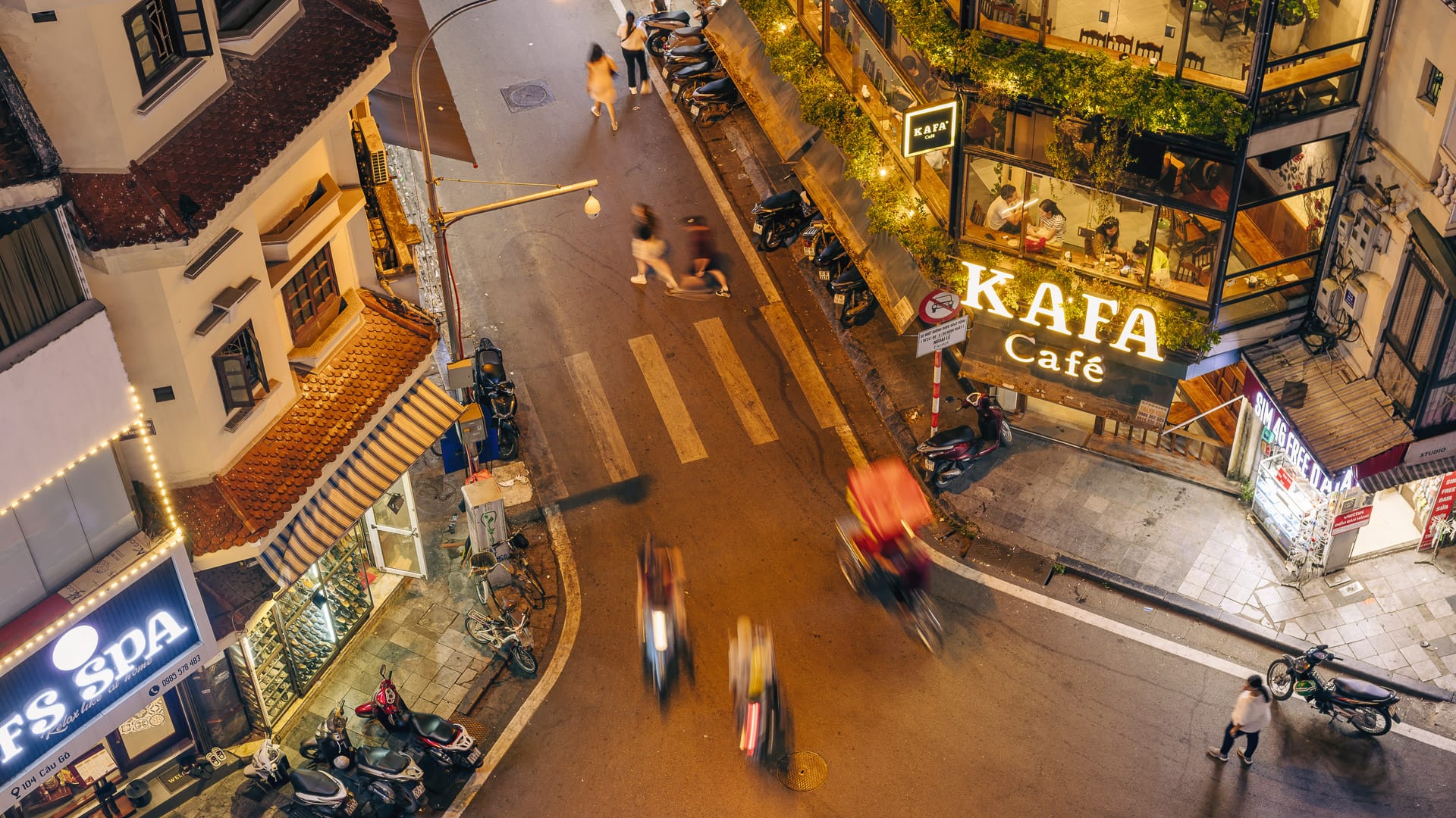 Overhead view of Hanoi street at night with blurred motion of bikes and glowing café signs