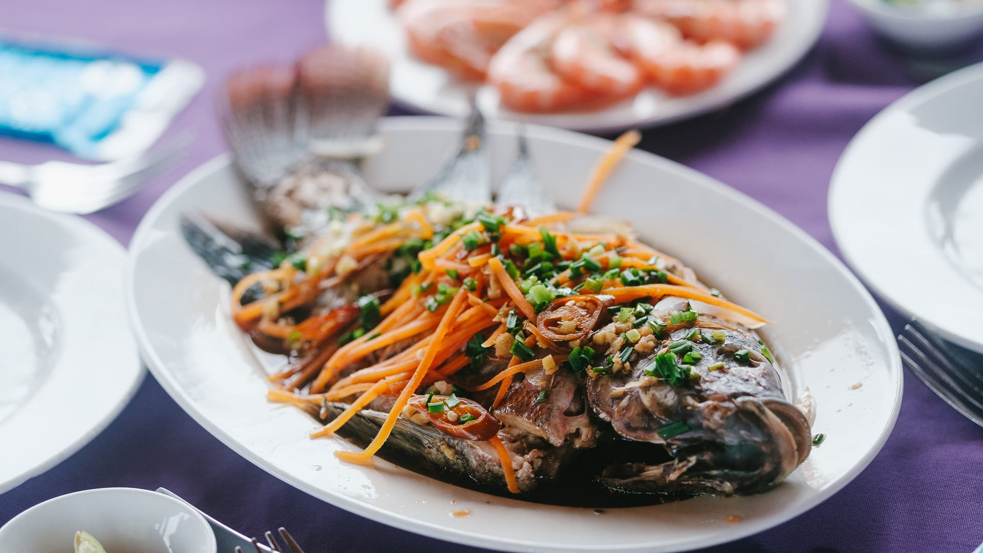 Vietnamese fish dish garnished with carrots and herbs on a white plate