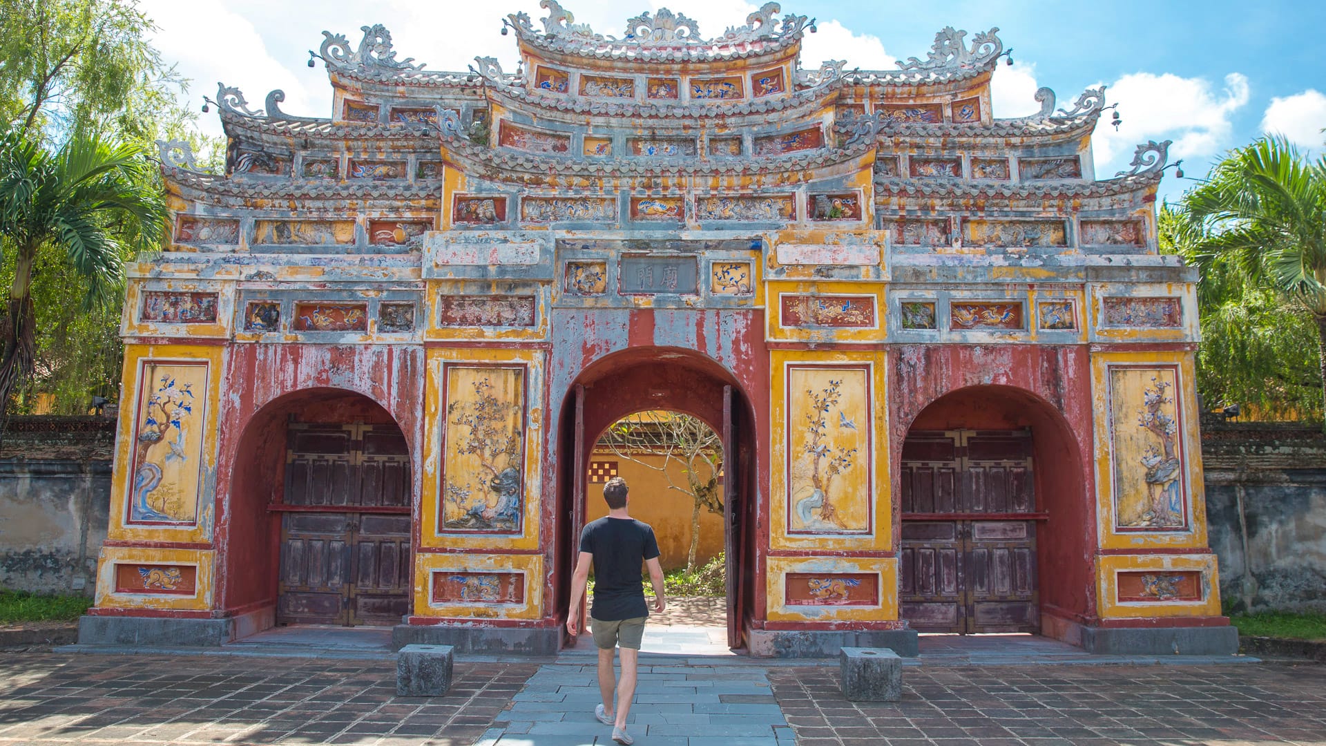 Traveller walking toward ornate red and gold gate at the Imperial City in Hue, Vietnam