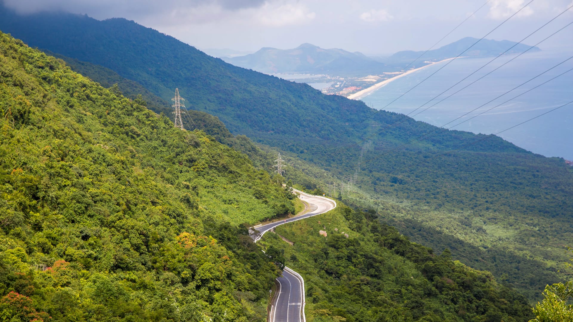 Winding road through lush green hills of the Hai Van Pass with coastline and sea in the distance
