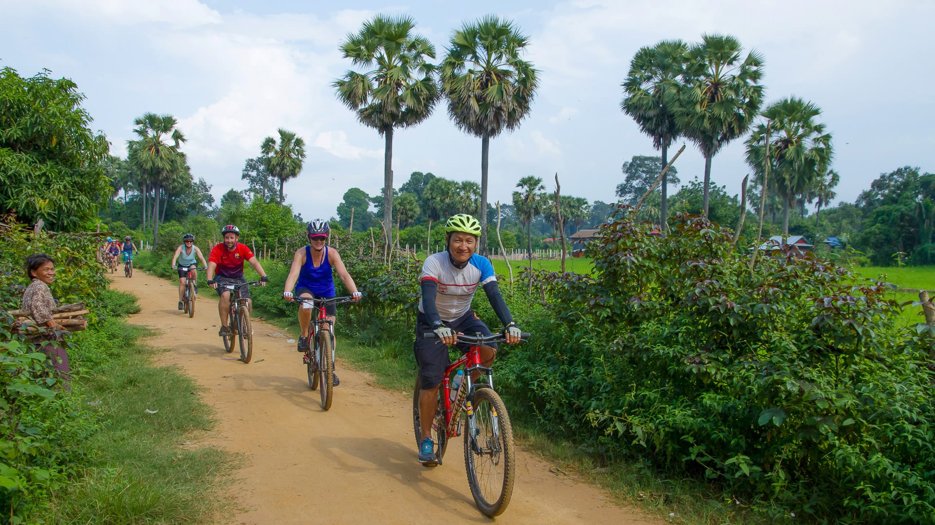 Cyclists riding a dirt trail flanked by palm trees in rural Vietnam