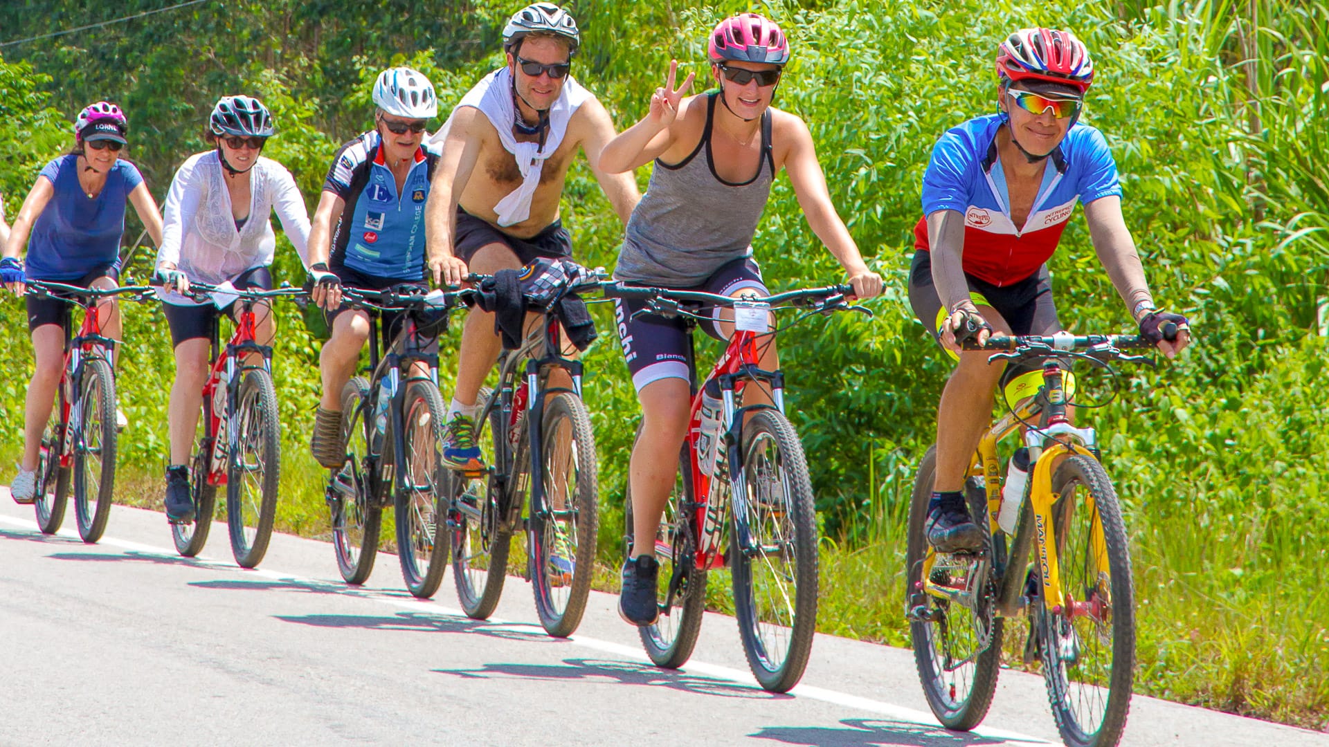 roup of cyclists riding along a sunlit rural road in Vietnam surrounded by green vegetation