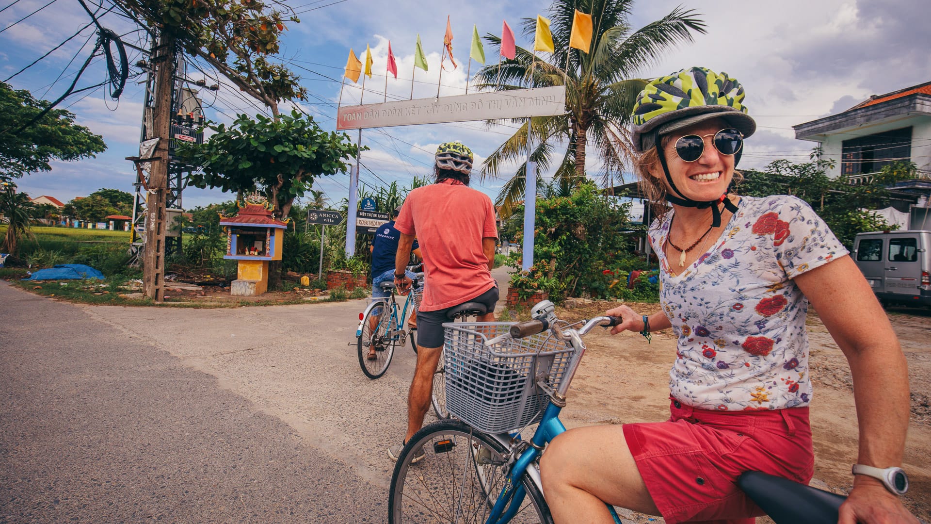 Woman smiling on a bicycle in Hoi An with tropical flags and palm trees in the background