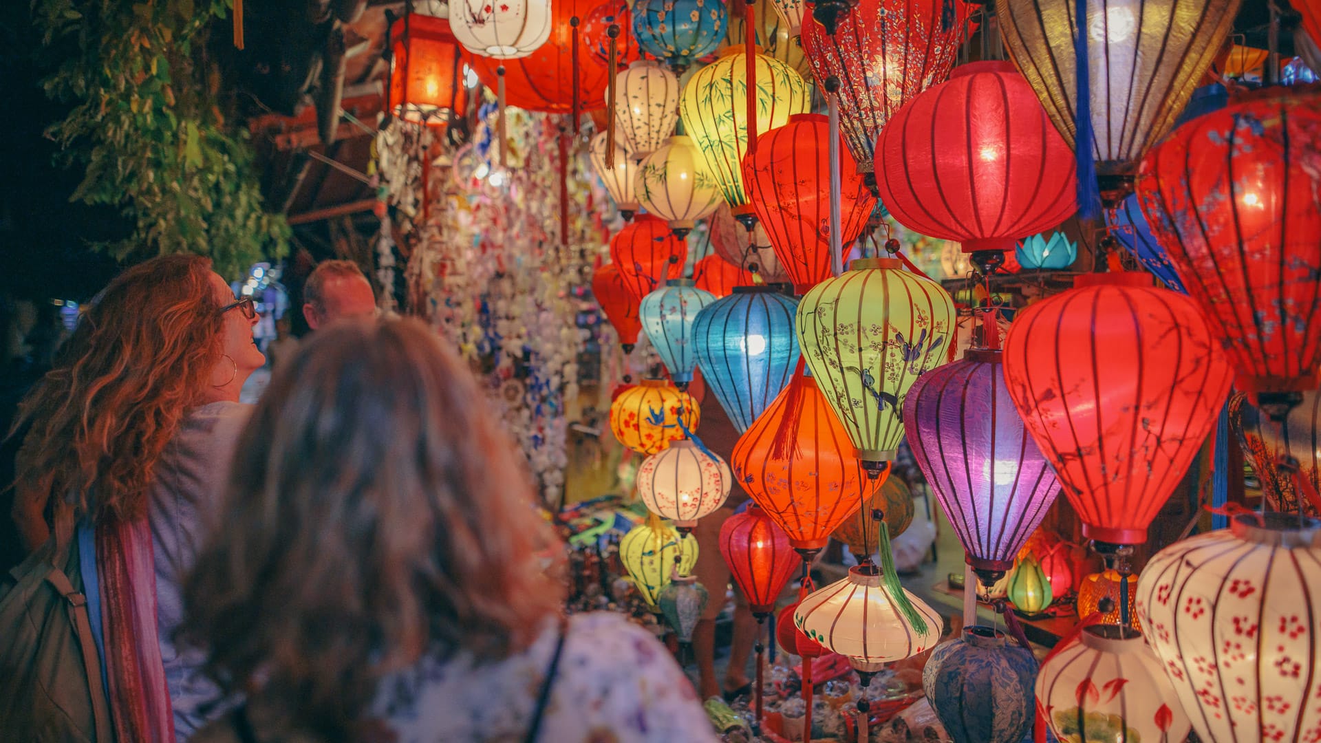 People browsing vibrant lanterns at a night market in Hoi An, Vietnam
