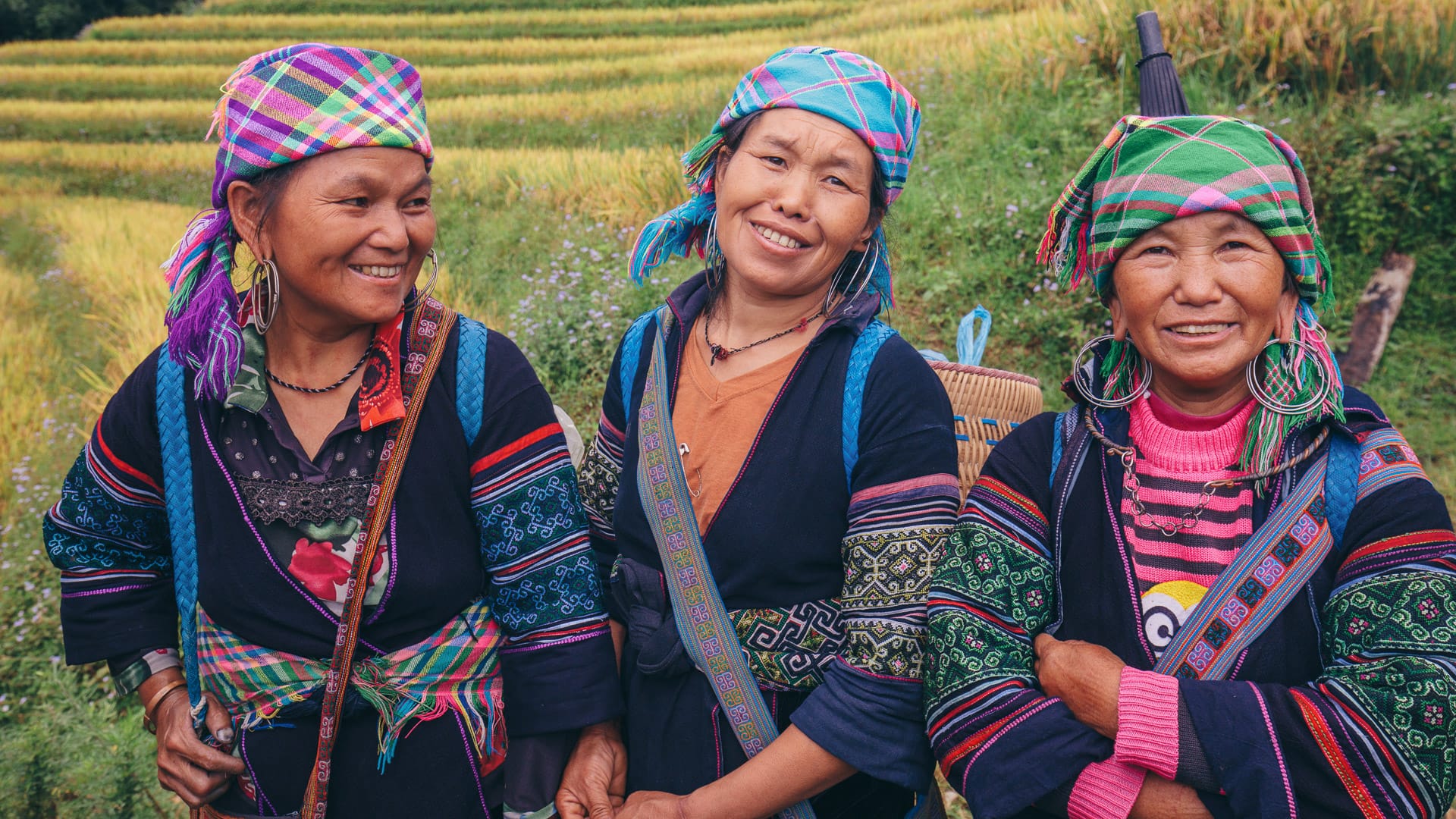 Three smiling women in colourful ethnic dress in Sapa rice fields
