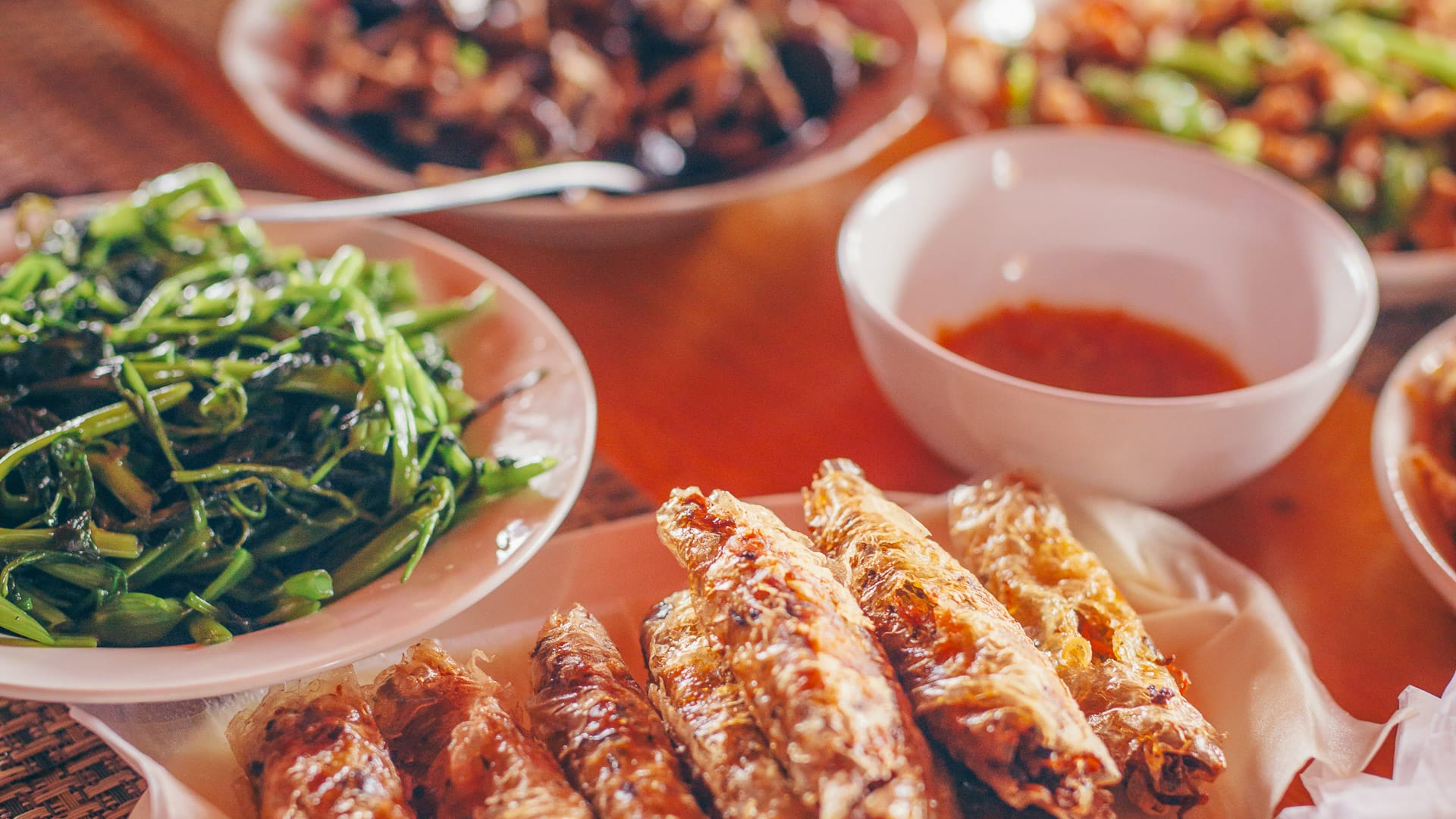Vietnamese meal with crispy spring rolls, sautéed greens and dipping sauce served on a wooden table