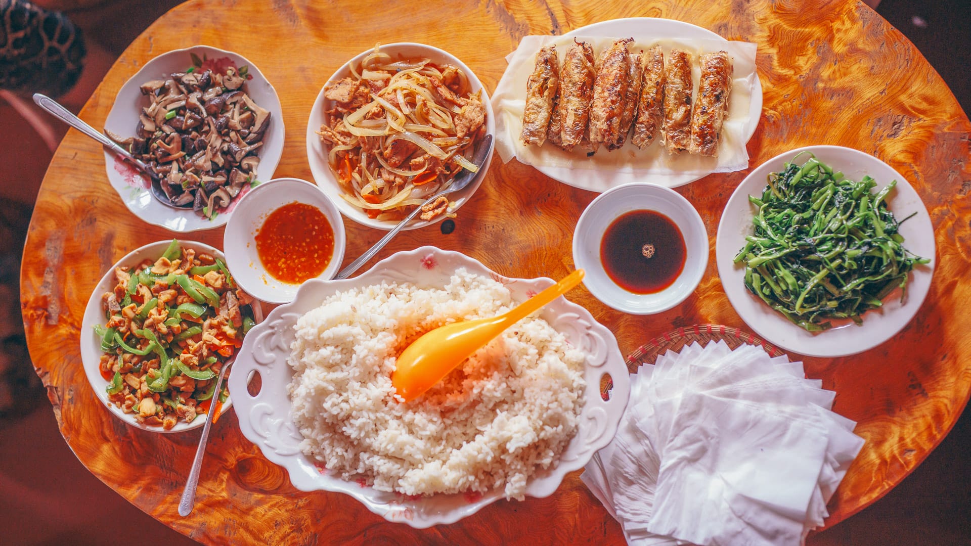 Top view of traditional Vietnamese dishes including rice, spring rolls and sautéed vegetables on round table