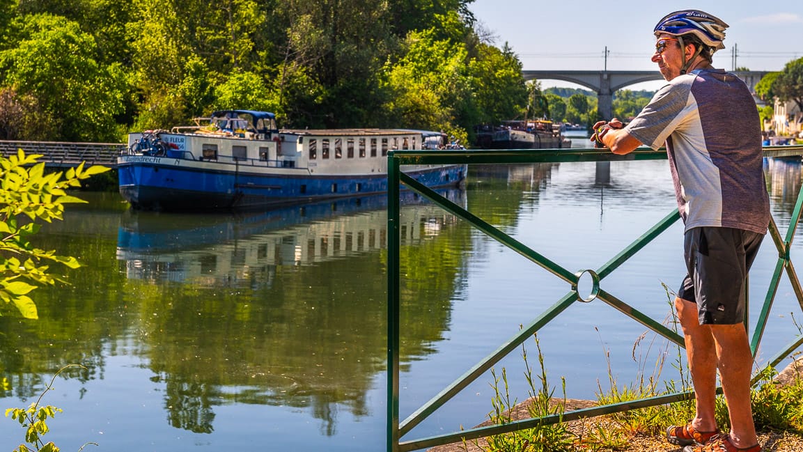 Fietser kijkt naar rivier Yonne met het schip Fleur in Moet-sur-Loing. Fiets-vaarvakantie Moret-sur-Loing naar Auxerre van Boat Bike Tours.