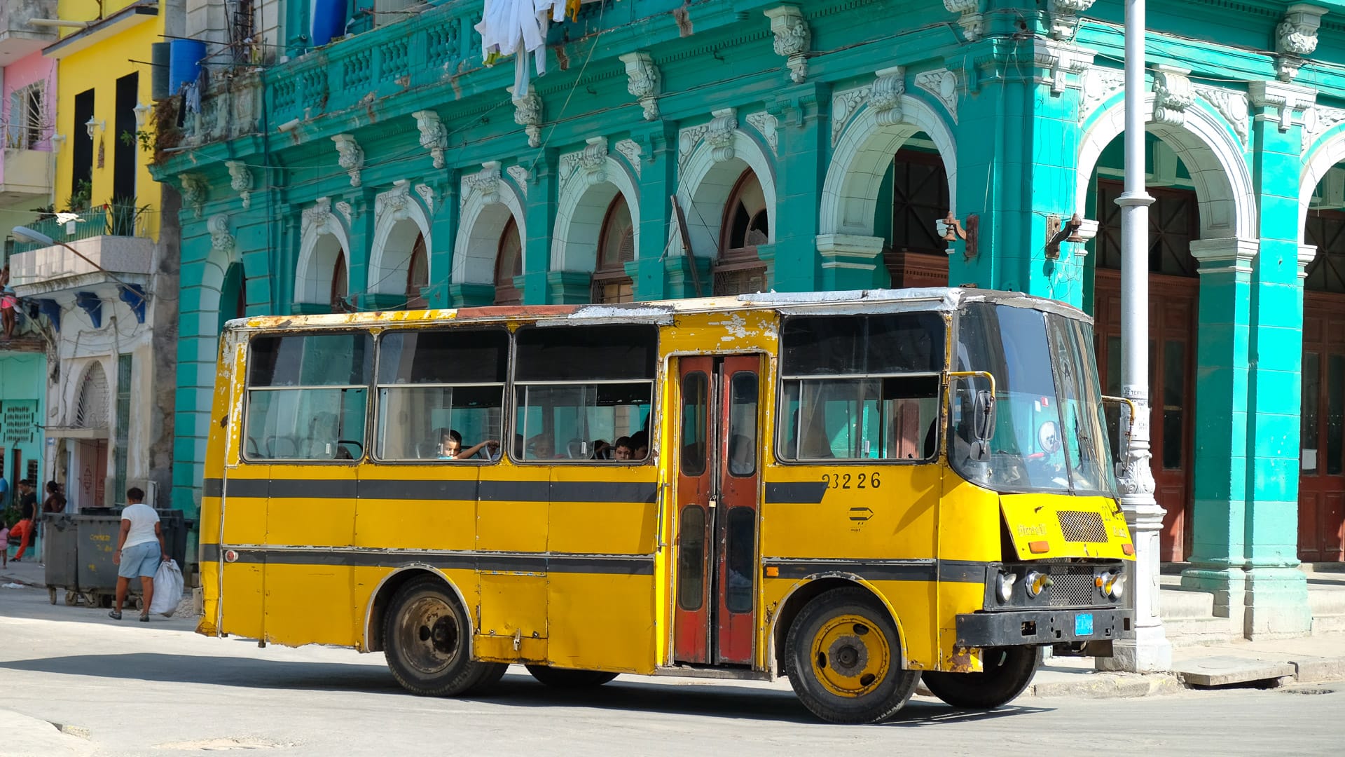 Bright yellow Cuban bus driving past colourful colonial buildings in central Havana