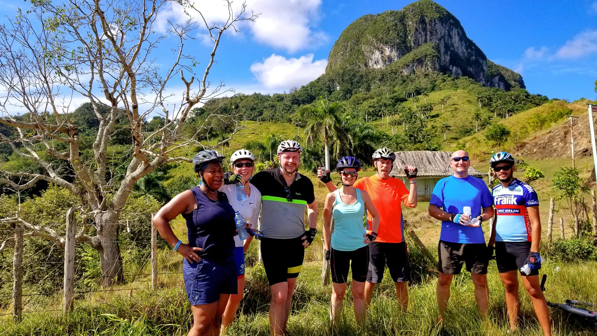 Group of cyclists posing with helmets in front of a dramatic limestone hill in rural Cuba