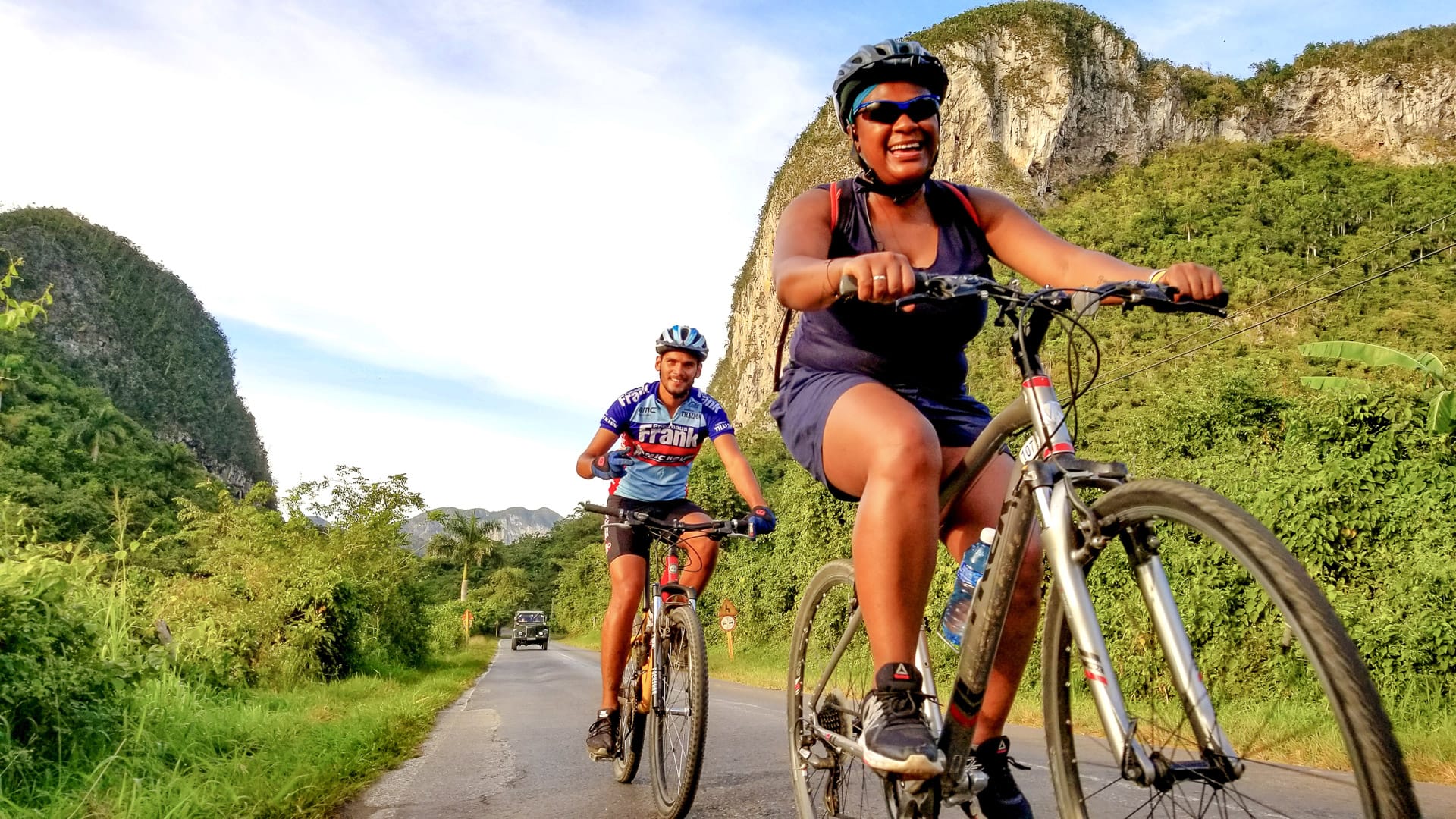 Smiling cyclists riding past lush limestone cliffs in Cuba