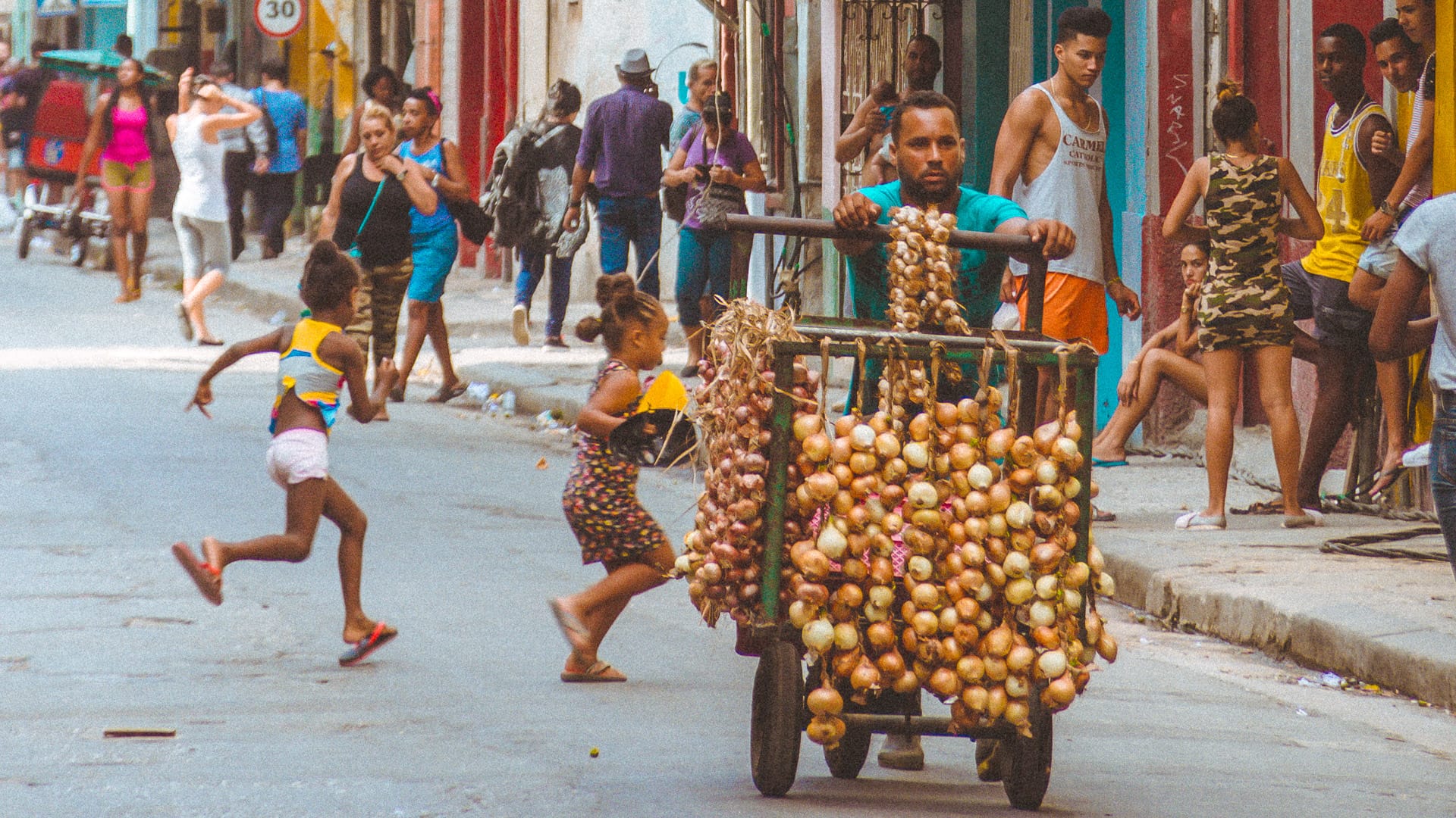 Cuban street vendor pushing a cart loaded with onions as children play around him