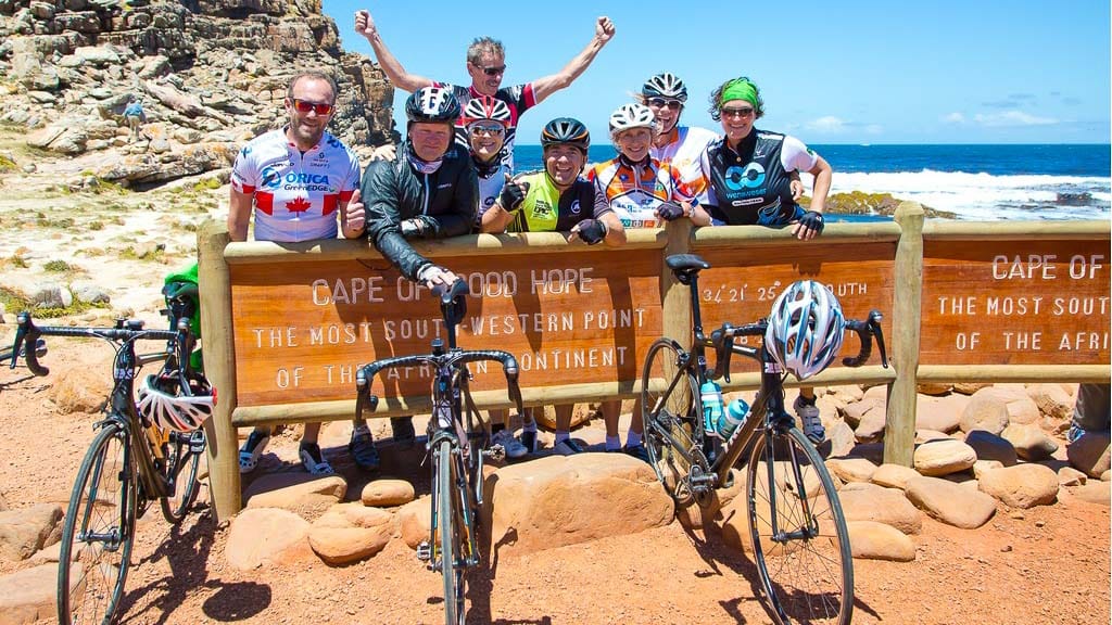 Group of cyclists pose with bikes at the Cape of Good Hope sign on a sunny day in South Africa