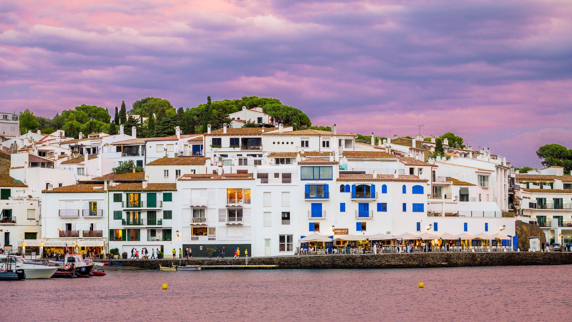 Waterfront view of whitewashed houses in Cadaqués, Catalonia at sunset with purple sky