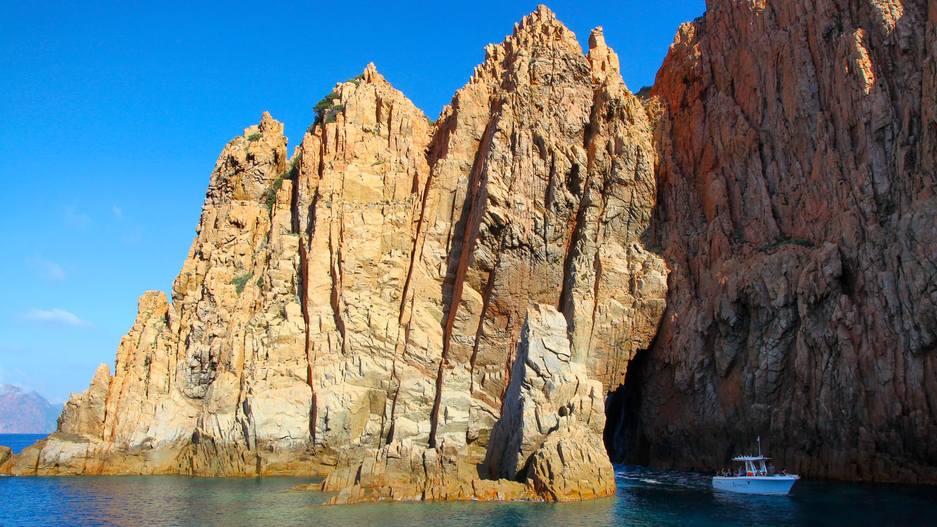 Boat entering a sea cave beneath red cliffs