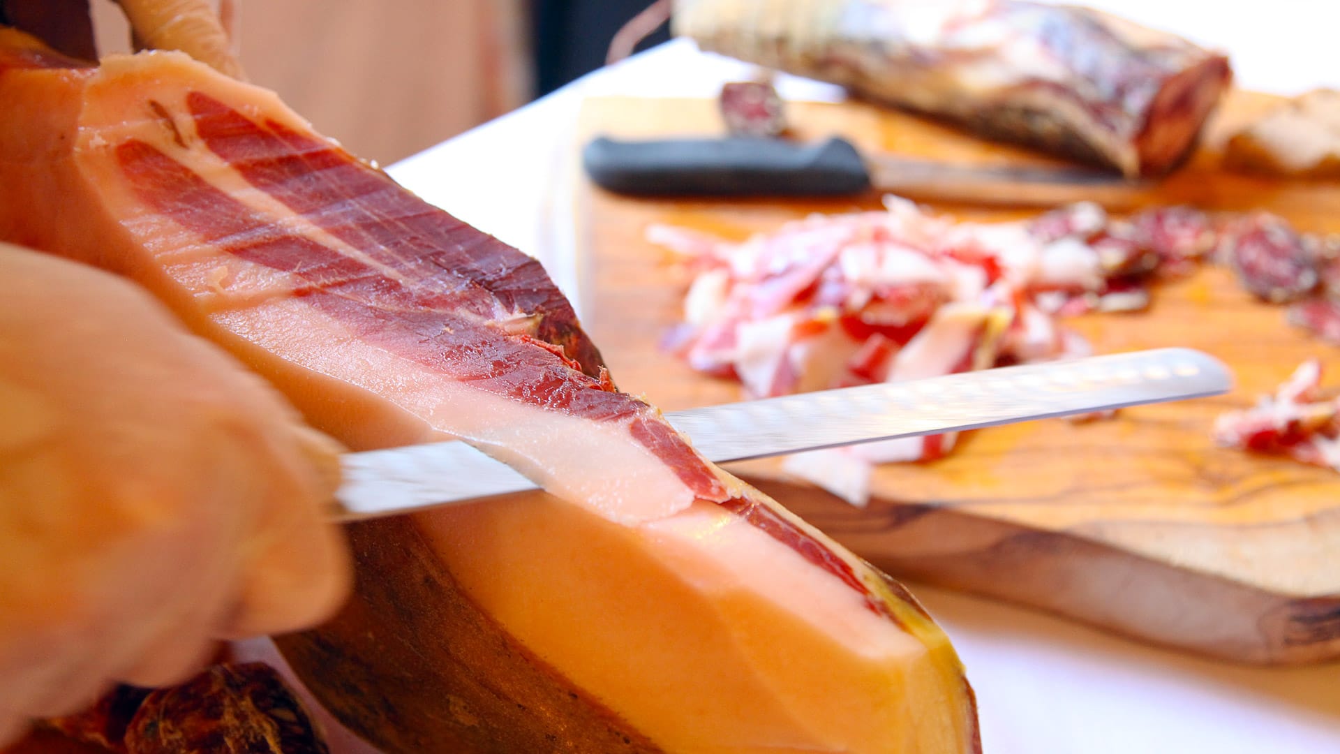 Close-up of Corsican charcuterie being hand-sliced from a cured ham on a wooden board