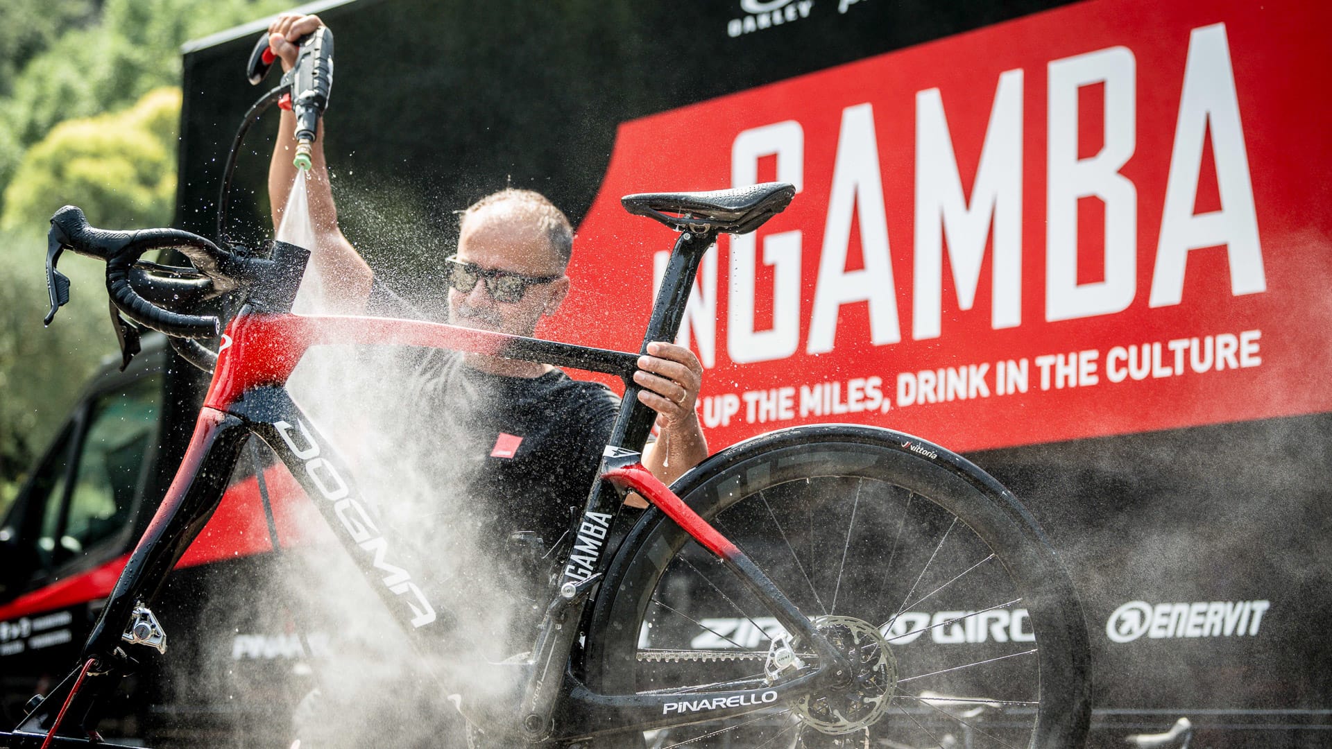 Man spraying down a red and black Dogma bike outside inGamba support van