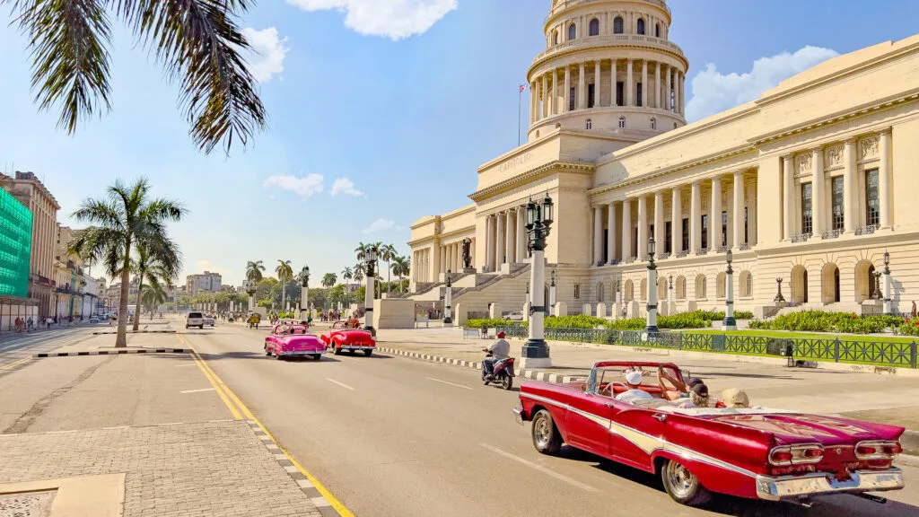 Convertible cars driving on the street in front of El Capitolio building in Cuba, Havana
