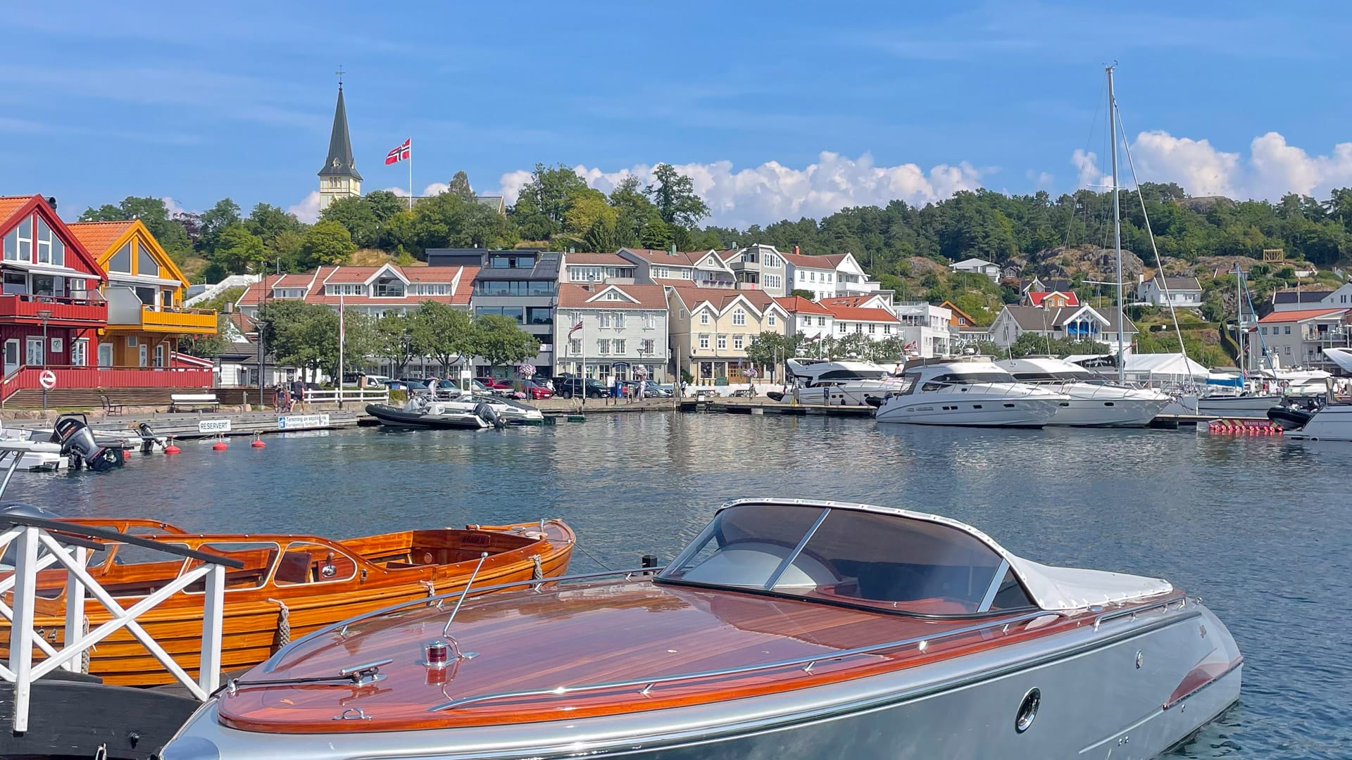 Wooden and luxury boats docked at Grimstad harbour with church spire and town buildings in background