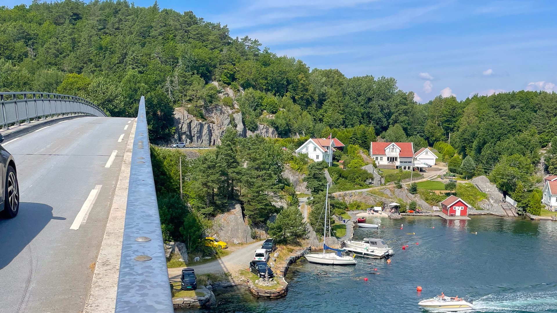 Bridge leading to Brekkestø over blue water, surrounded by rocky cliffs and forested hills