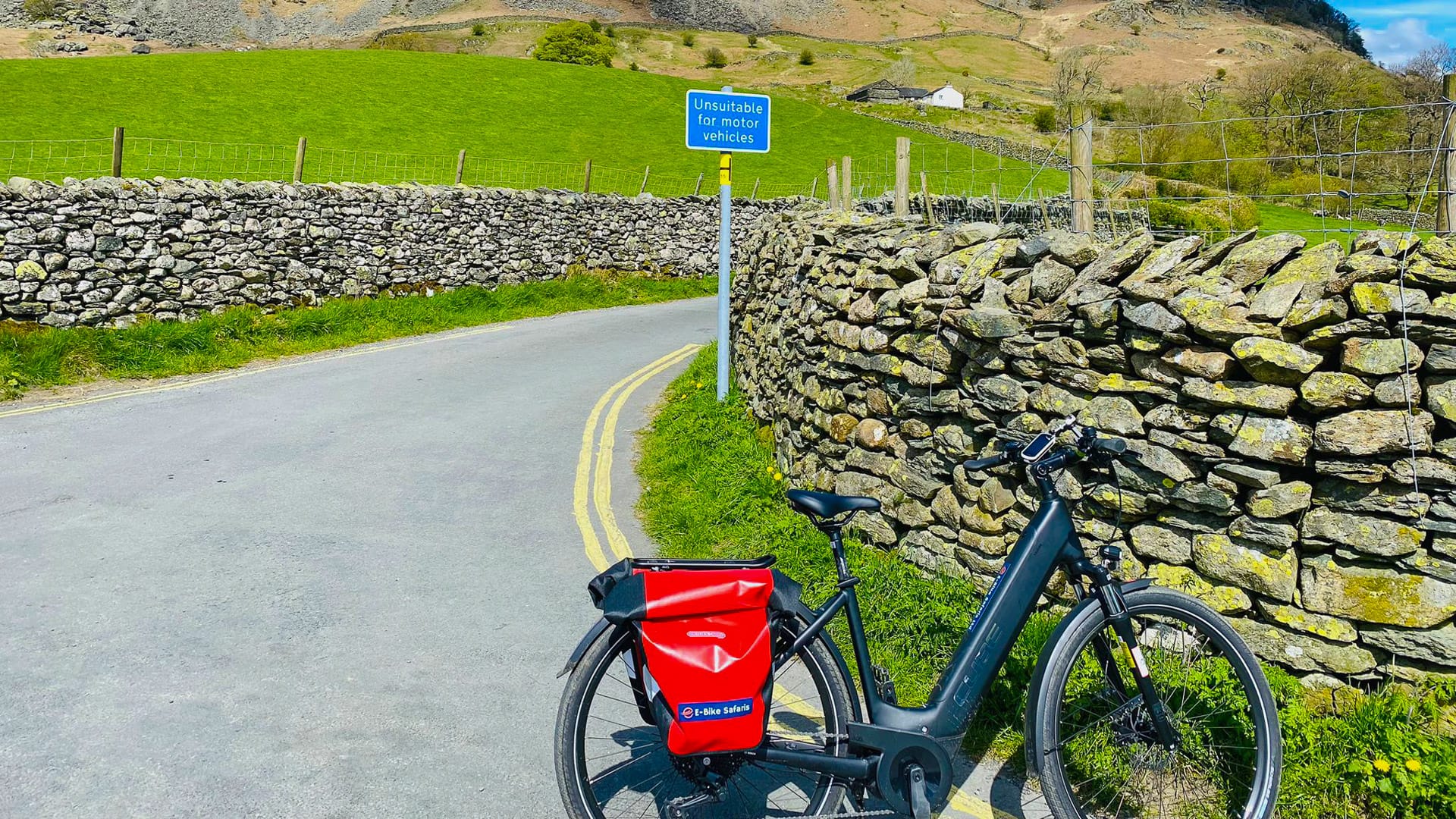 Electric bike with red pannier beside stone wall on country lane in Langdale Valley