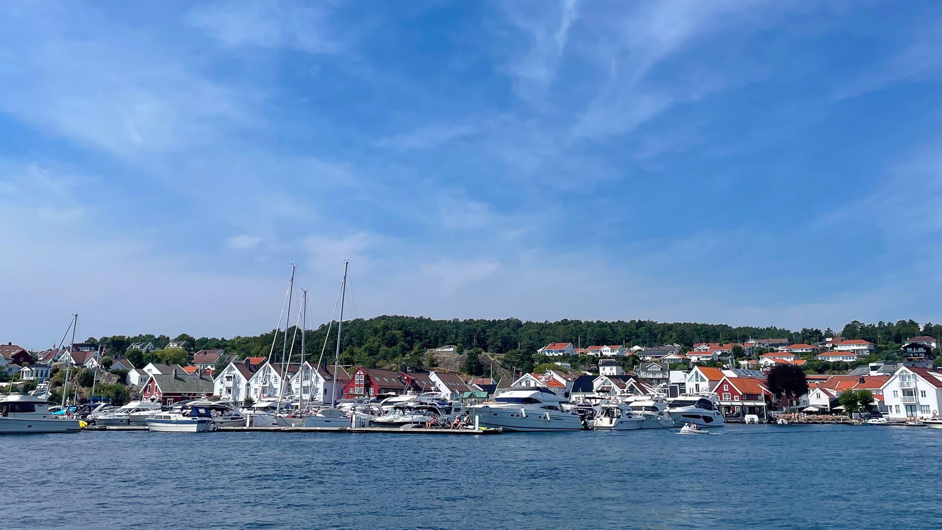 Sailboats and houses along the waterfront at Lillesand under a bright blue summer sky