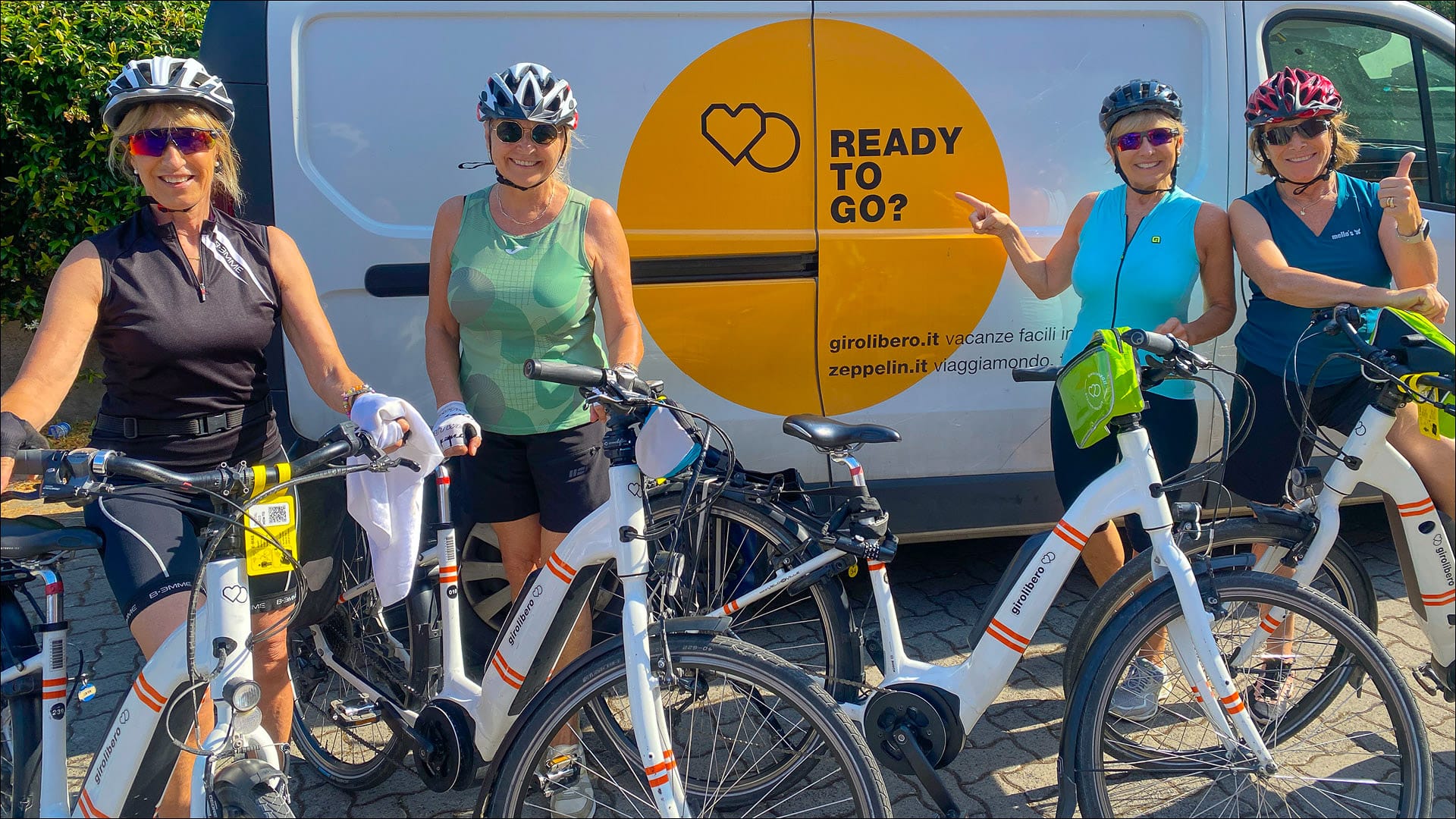 Four cyclists smiling with their bikes in front of a van