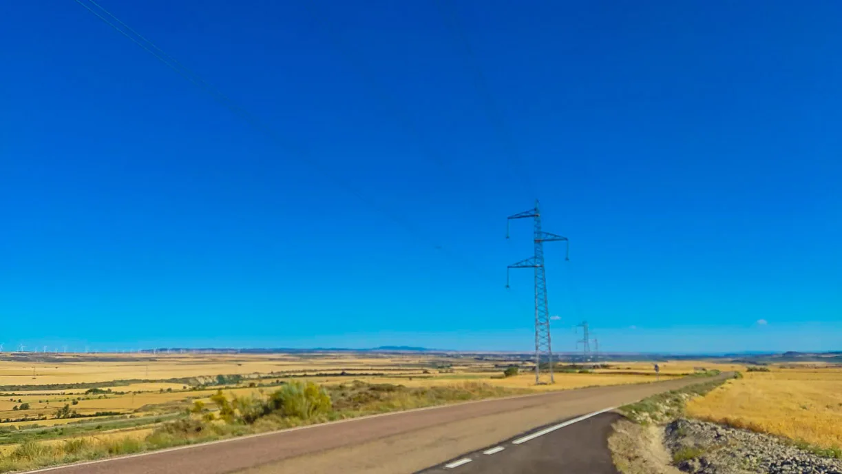 Straight road through golden plains with power lines under vivid blue sky near Zaragoza