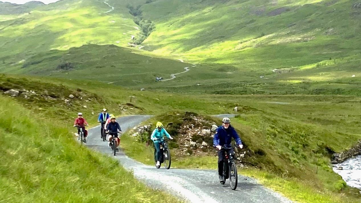 Group of cyclists climbing a winding road through open green hills in the Lake District