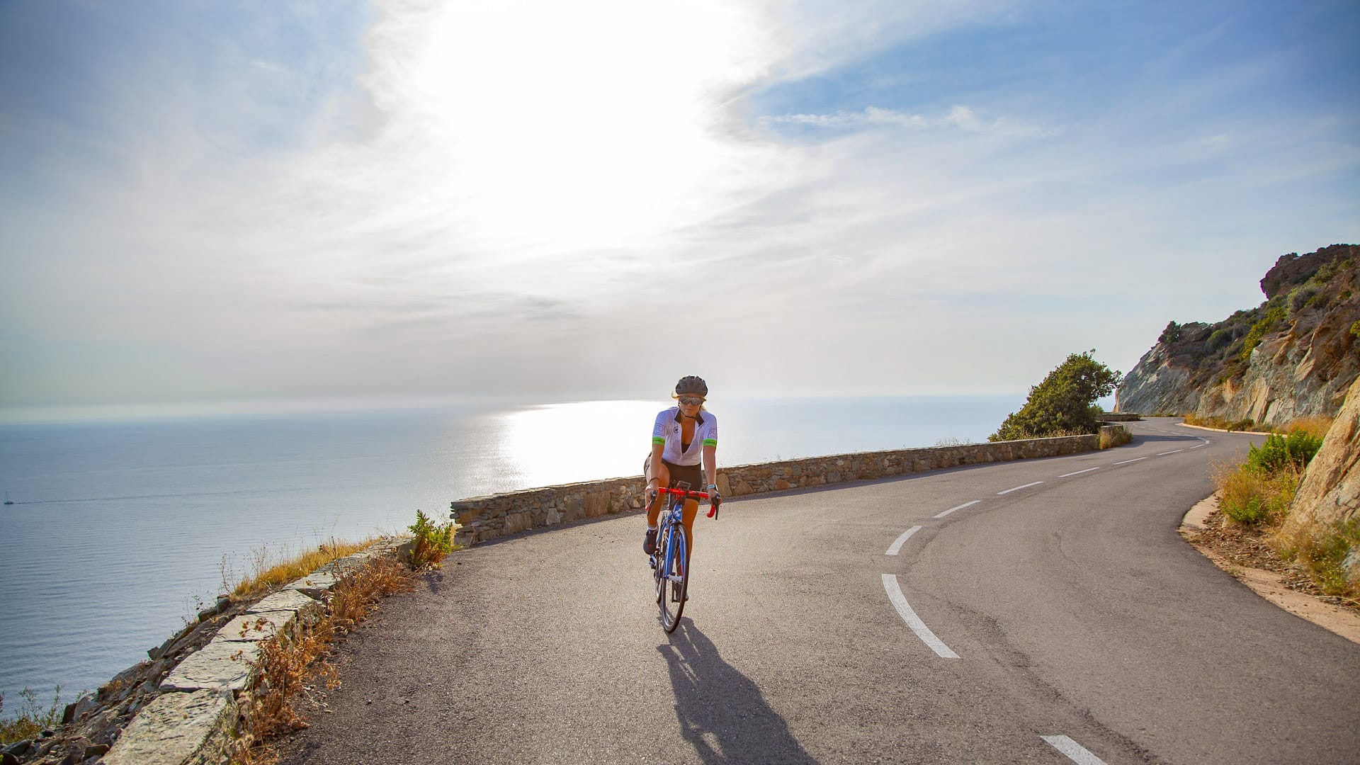 Road cyclist riding coastal bend above sparkling Corsican sea