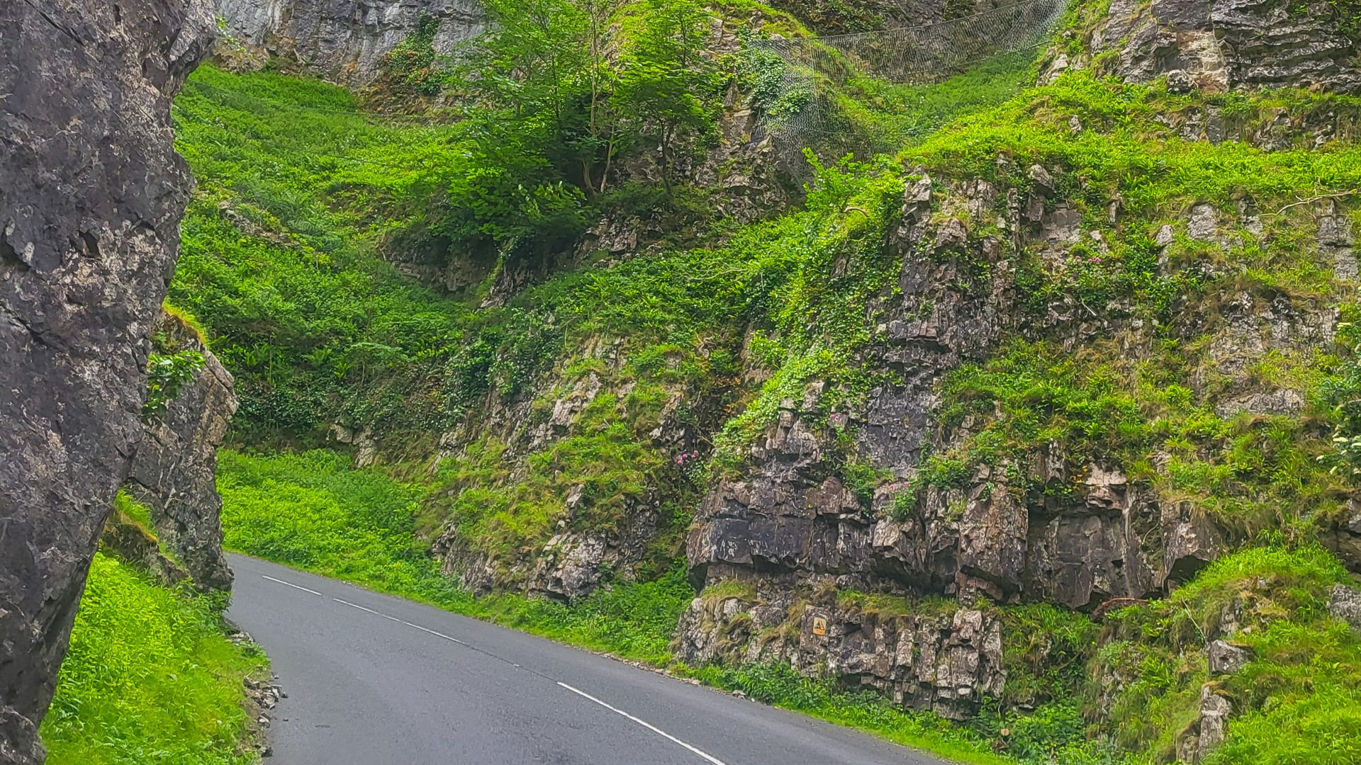 Narrow road winding between steep green cliffs and rocky outcrops in a gorge