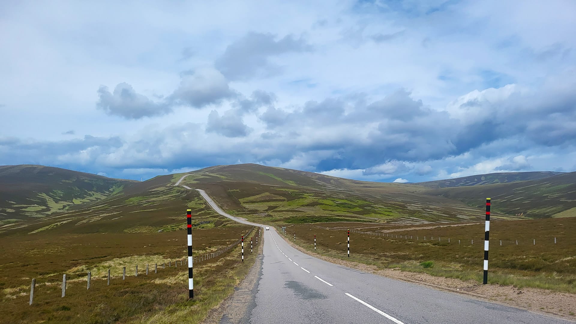 Open road through rolling hills under a cloudy blue sky on the Land’s End to John O’Groats route