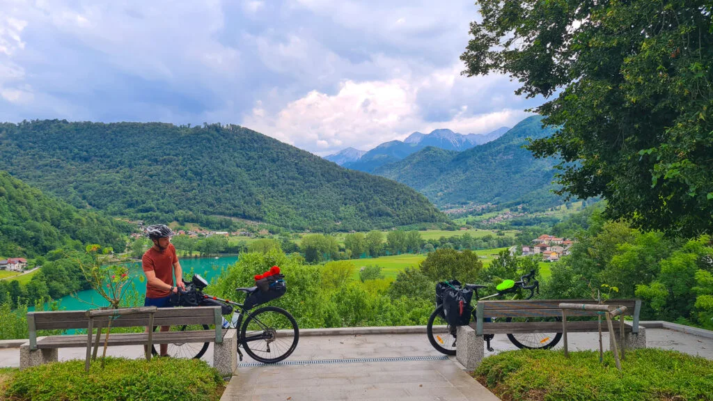 Bikepacker pauses at viewpoint over green valley and turquoise river in Slovenia