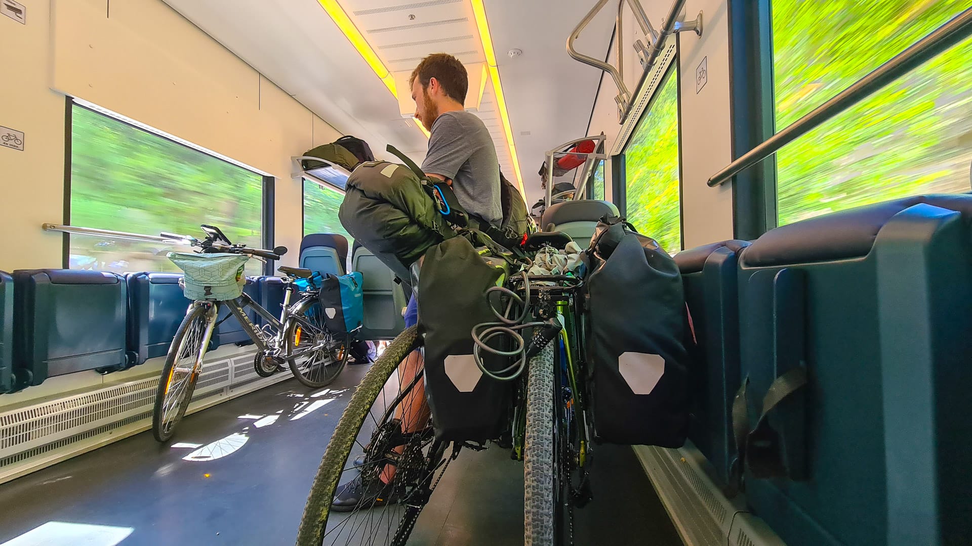 Cyclist sits beside loaded touring bike in train carriage during journey through Slovenia