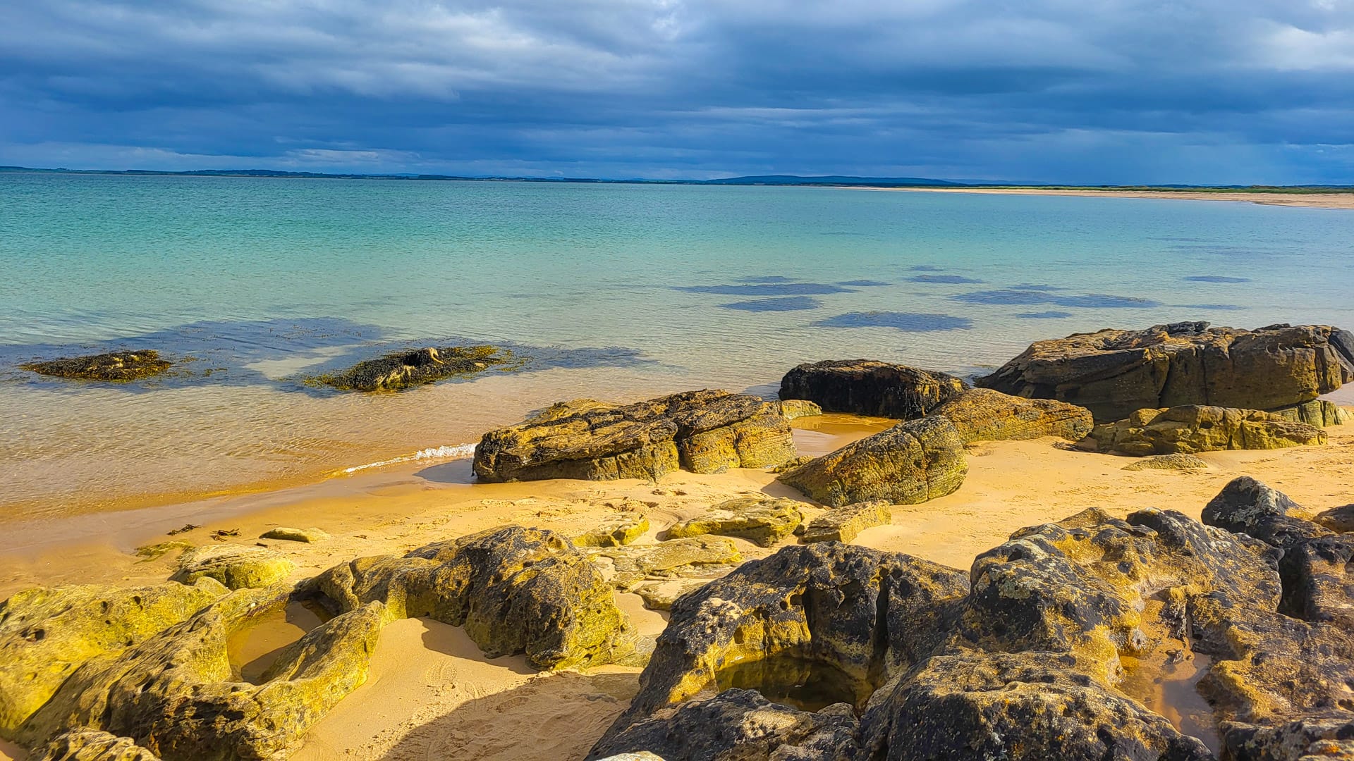 Golden sandy beach with turquoise water and rocky shoreline under a cloudy sky