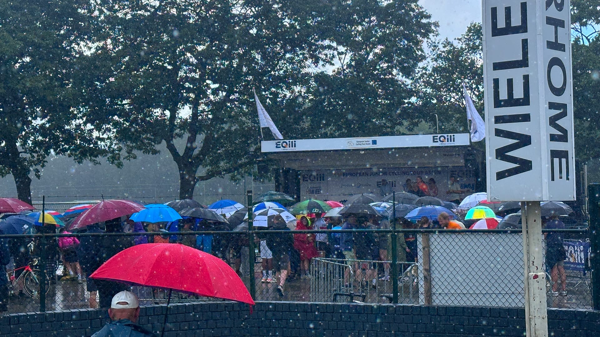 Spectators with umbrellas gathered in heavy rain near the final podium at the European Junior Cycling Tour