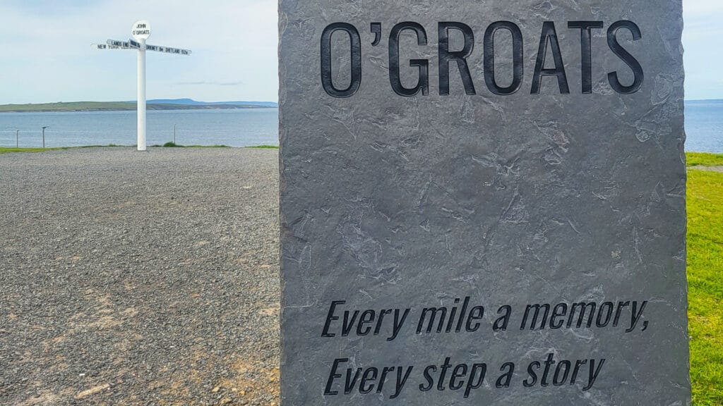 Stone marker at John O’Groats with engraved text and signpost in background