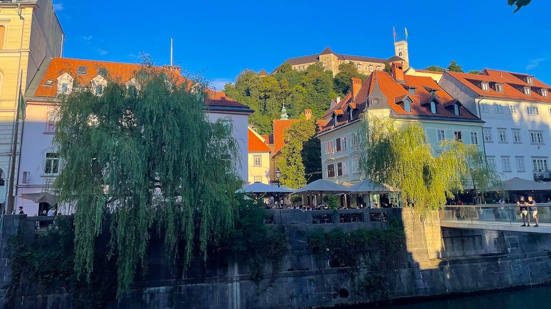 Ljubljana riverside cafés with castle on the hill above historic houses