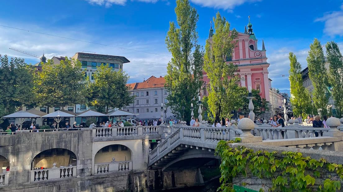 Ljubljana Triple Bridge with crowds and pink Franciscan church in the background