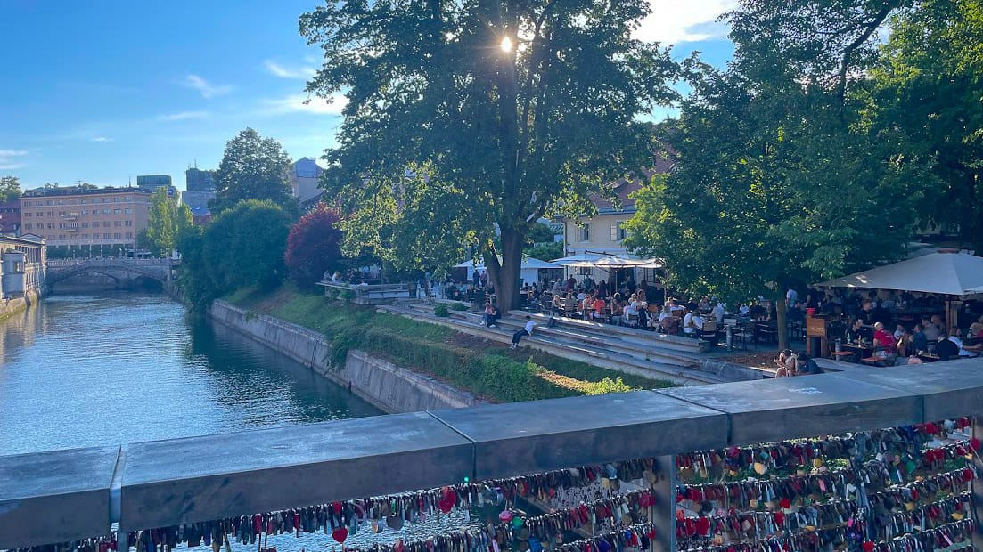 View from Ljubljana’s love lock bridge over river to lively riverside cafés and trees