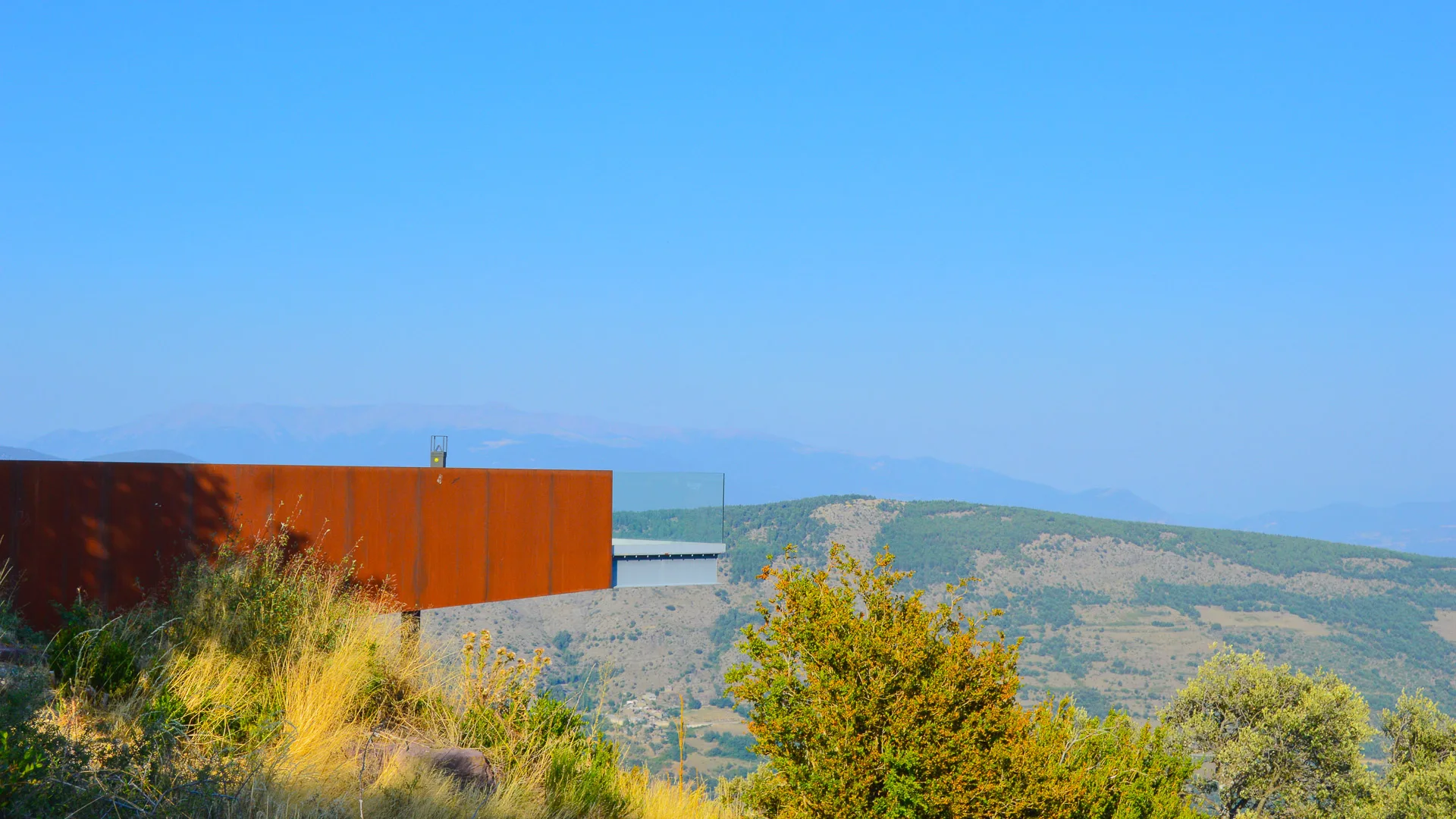 Modern viewpoint structure at Mirador Guils del Cantó overlooking rolling hills and distant mountains