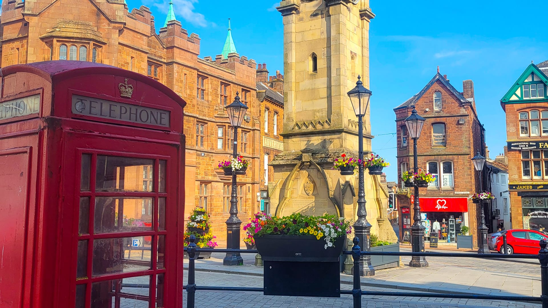 Historic clock tower with red telephone box and flower displays in a British market town