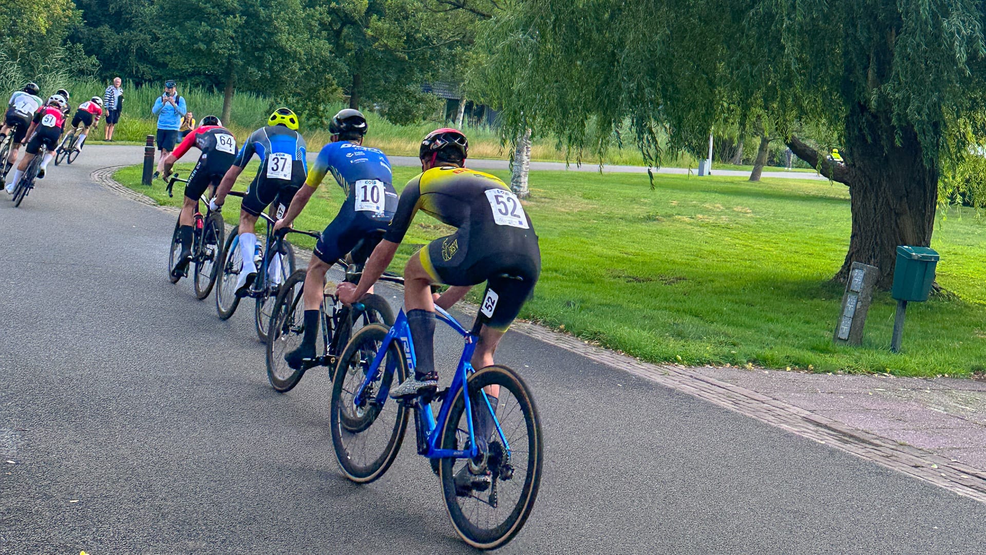 Junior cyclists racing in a tight group on a tree-lined road during a criterium near Assen