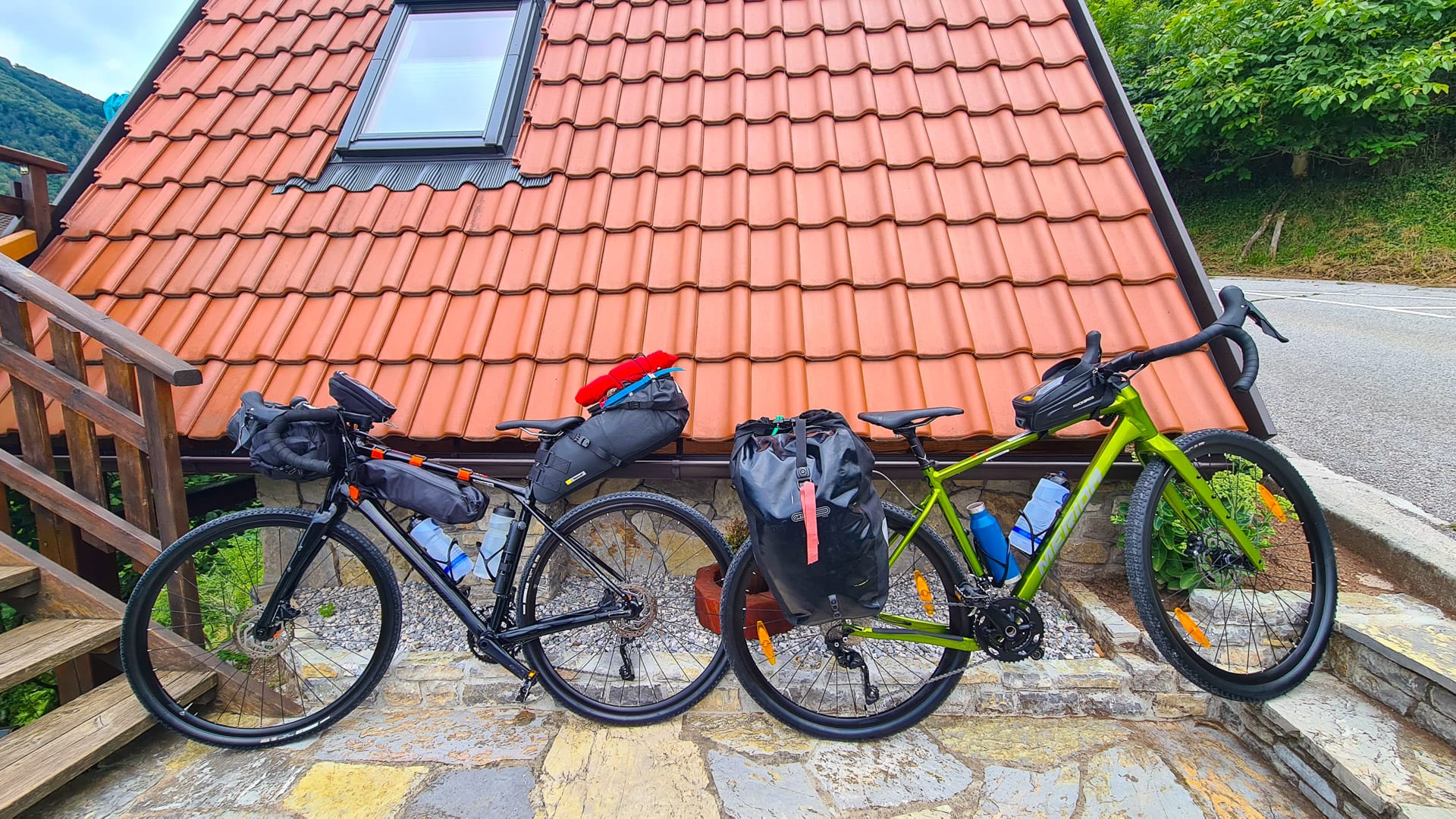 Two fully loaded gravel bikes parked against red-roofed hut in Slovenia