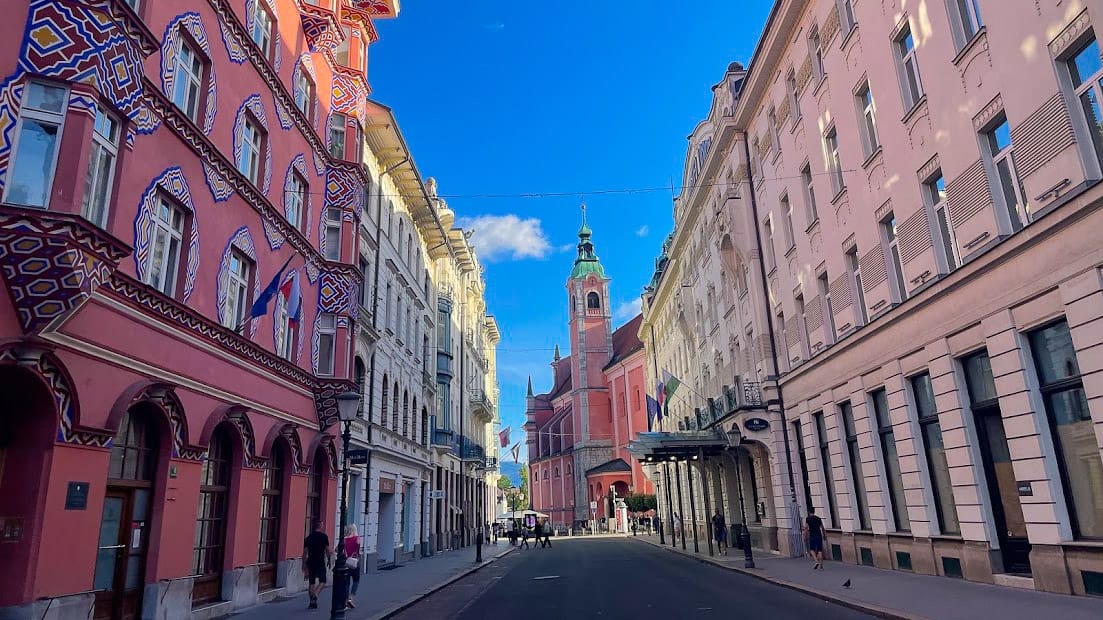 View of Franciscan church in Ljubljana framed by ornate pink and white buildings